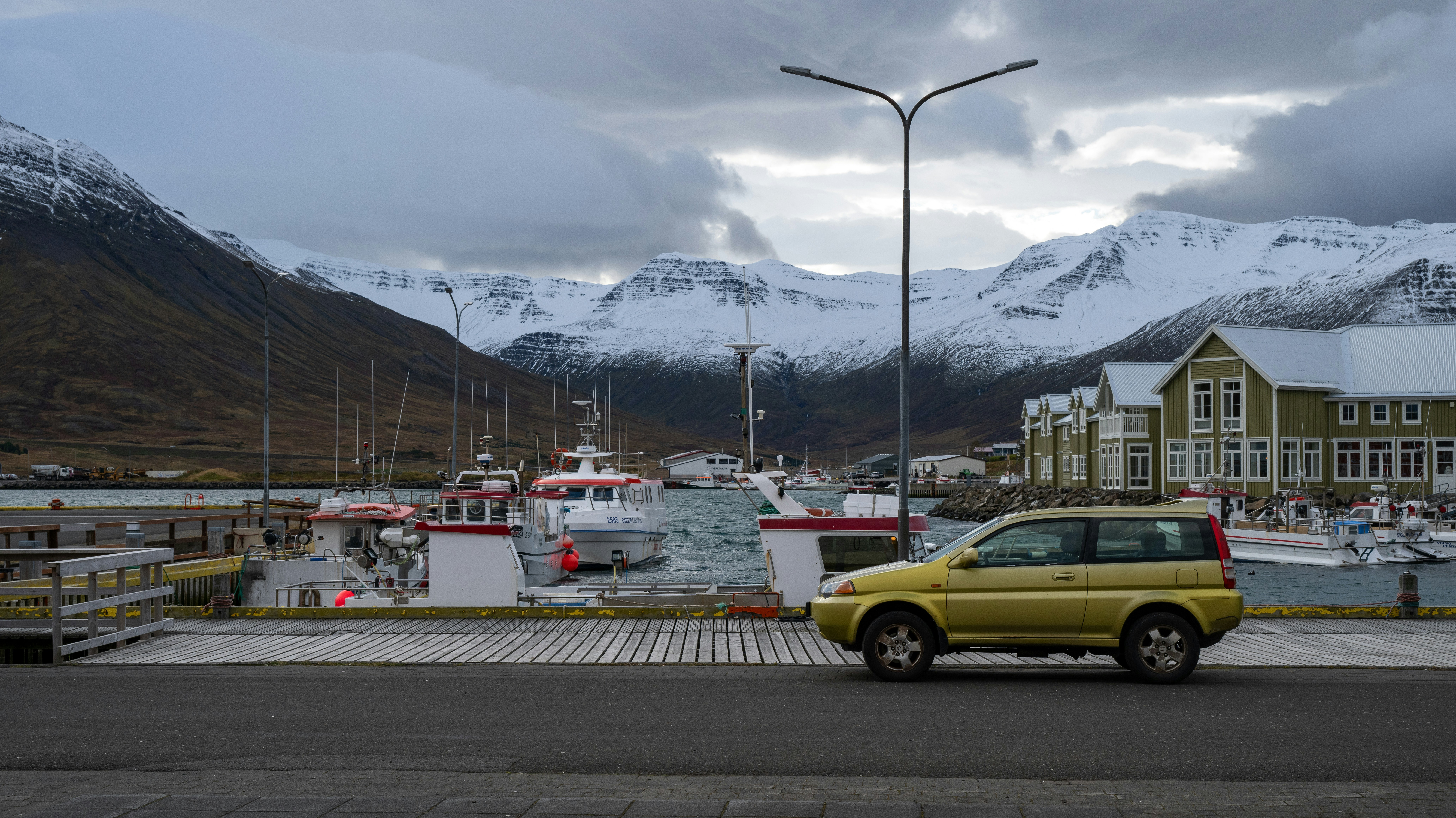 Car parked on a harbor with snow-capped mountains.