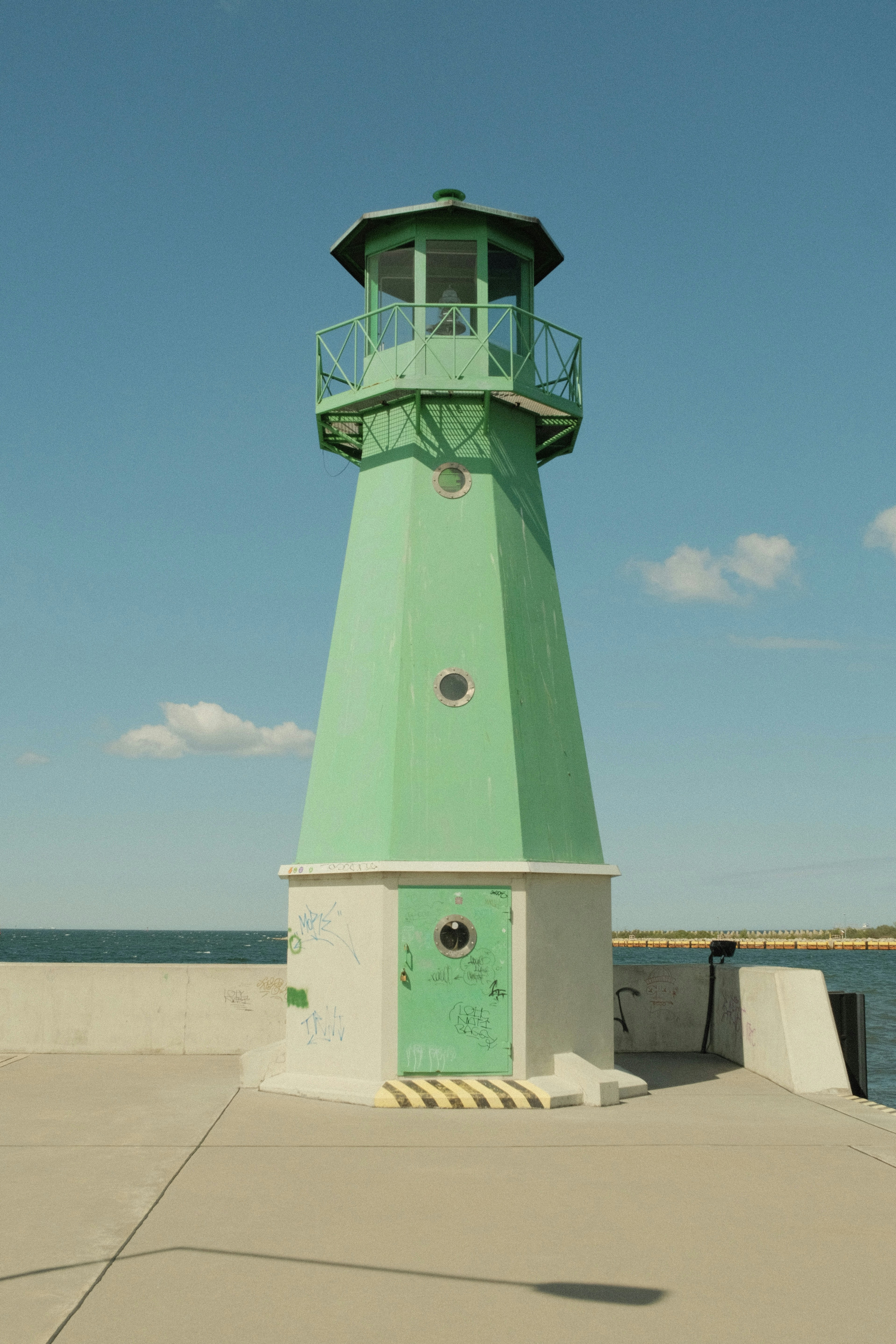 A green lighthouse stands tall against a blue sky.