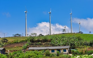 Wind turbines stand atop a green hill under a blue sky.
