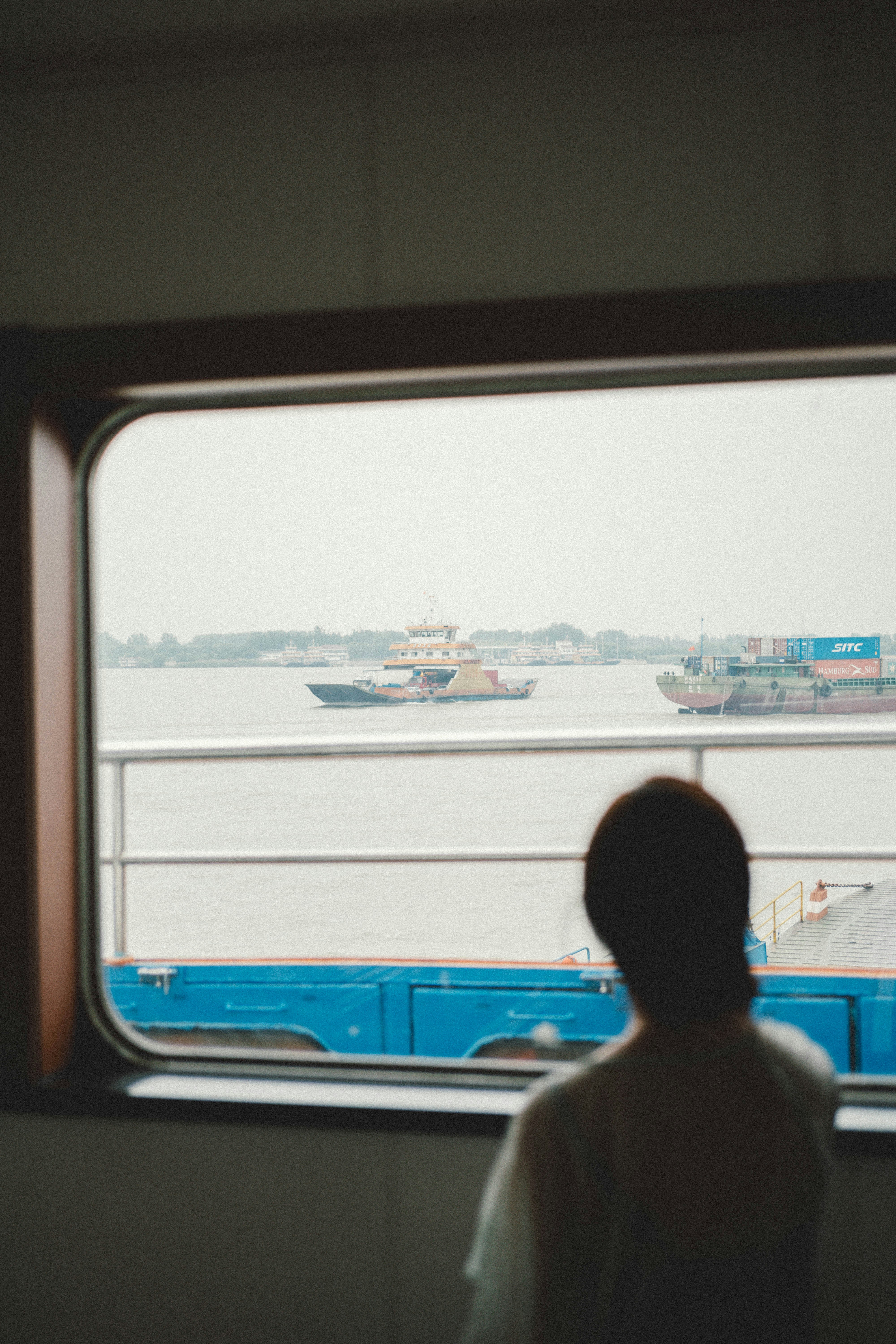 A person watches boats through a window.