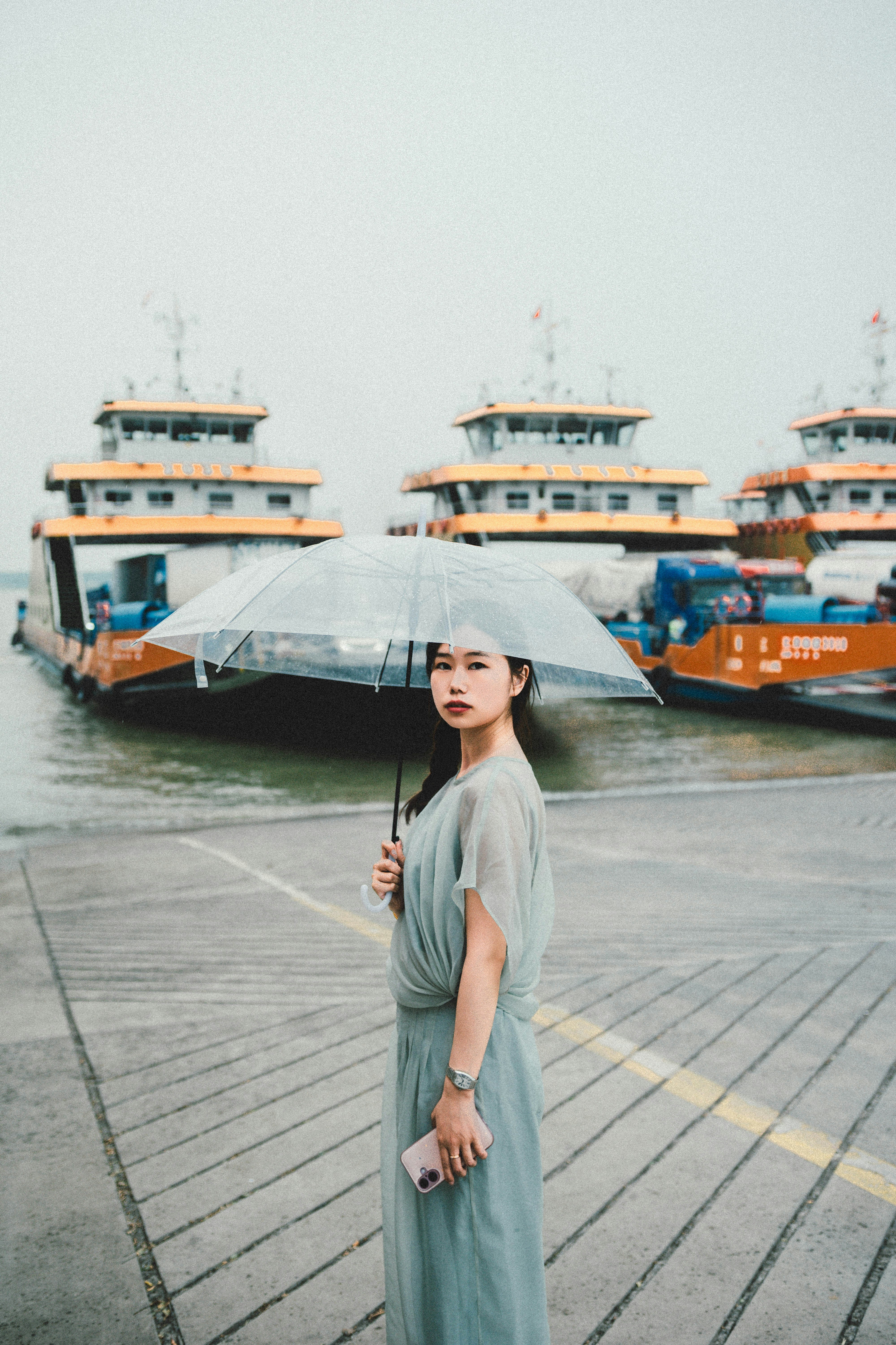 A woman poses by boats with an umbrella.