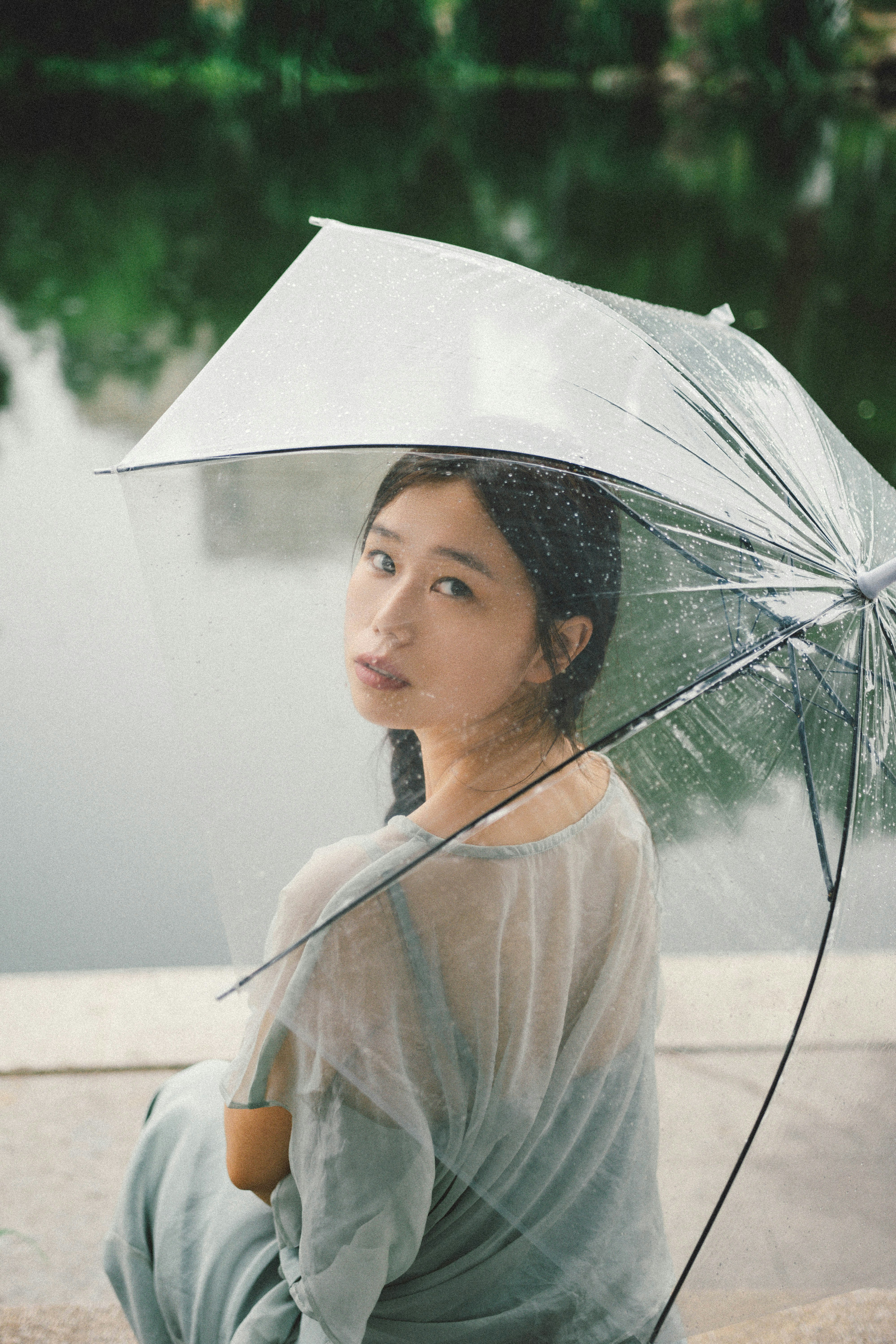 透明な傘の下で静かに座る女性