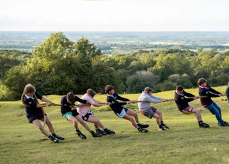 People are playing tug-of-war on a grassy hillside.