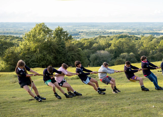People are playing tug-of-war on a grassy hillside.