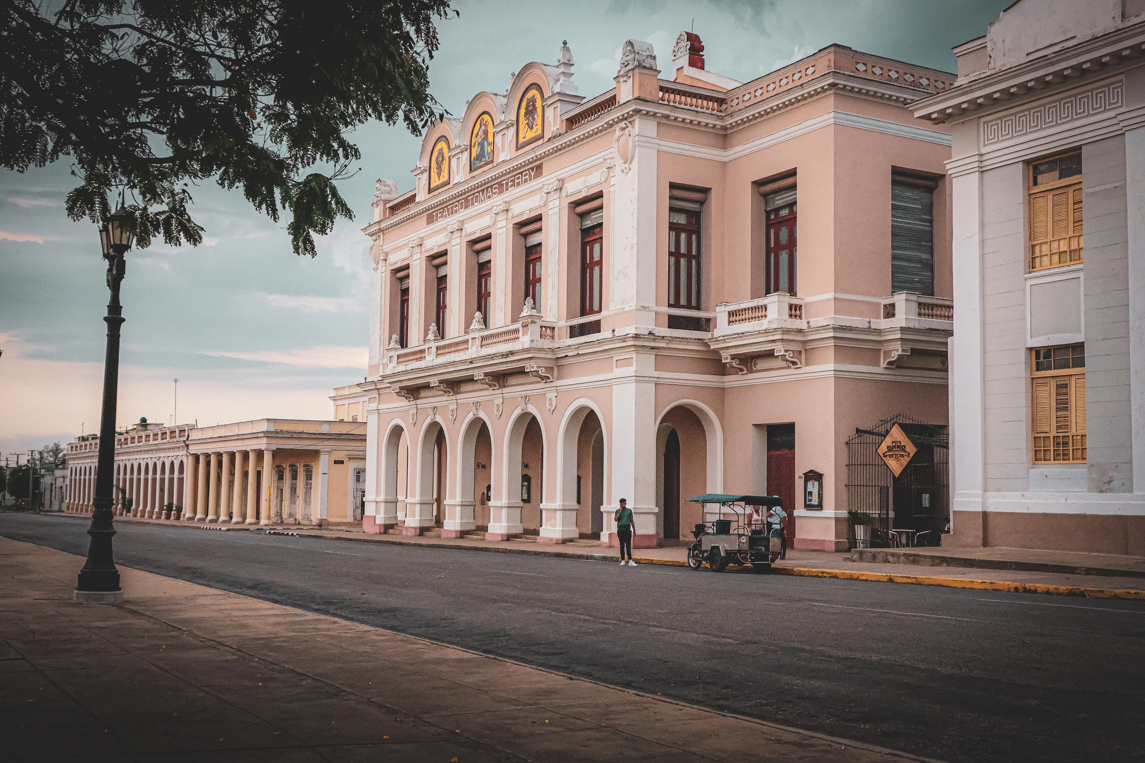 A colonnaded historic building on a quiet street in Cienfuegos