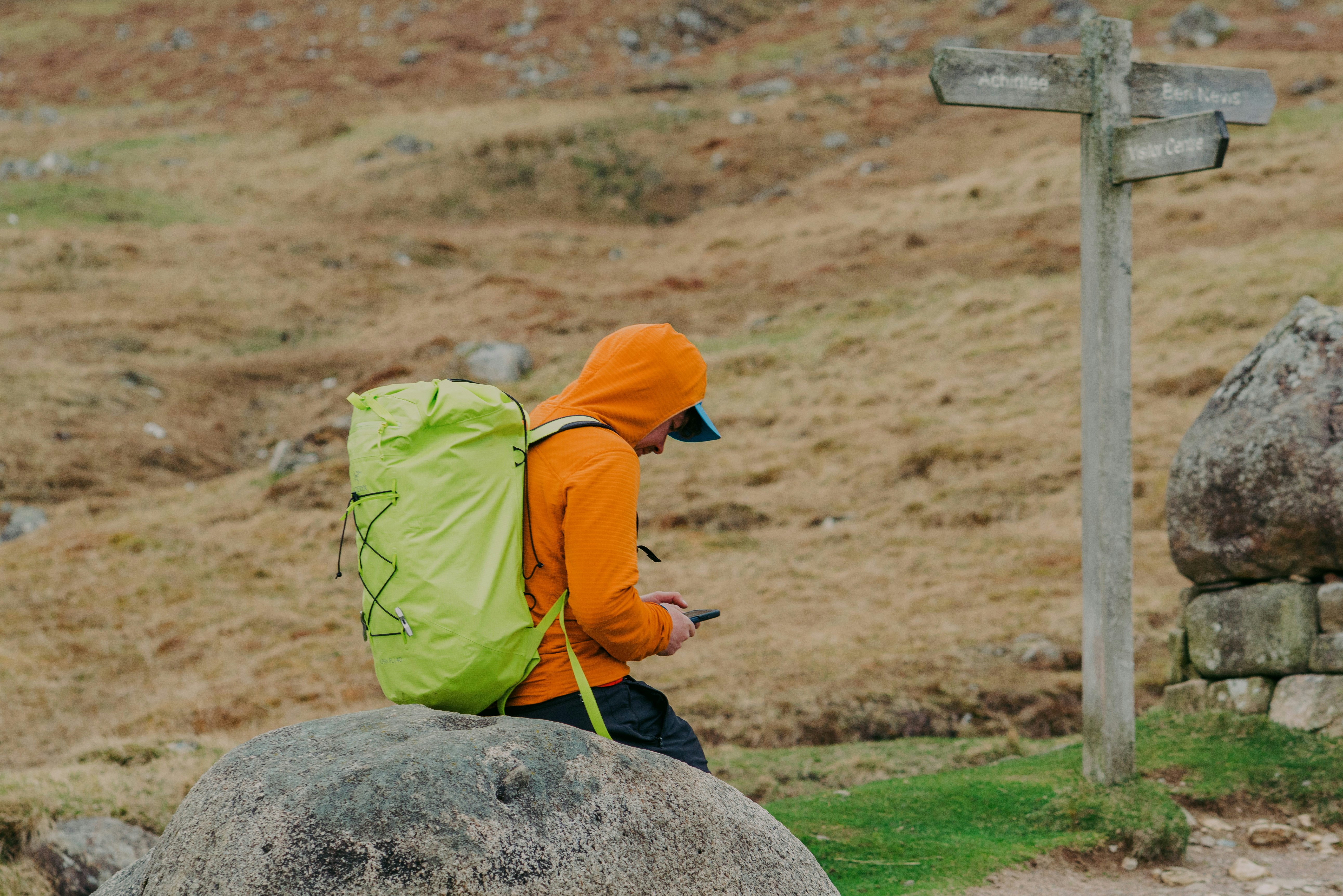 A hiker consults their phone by a signpost.