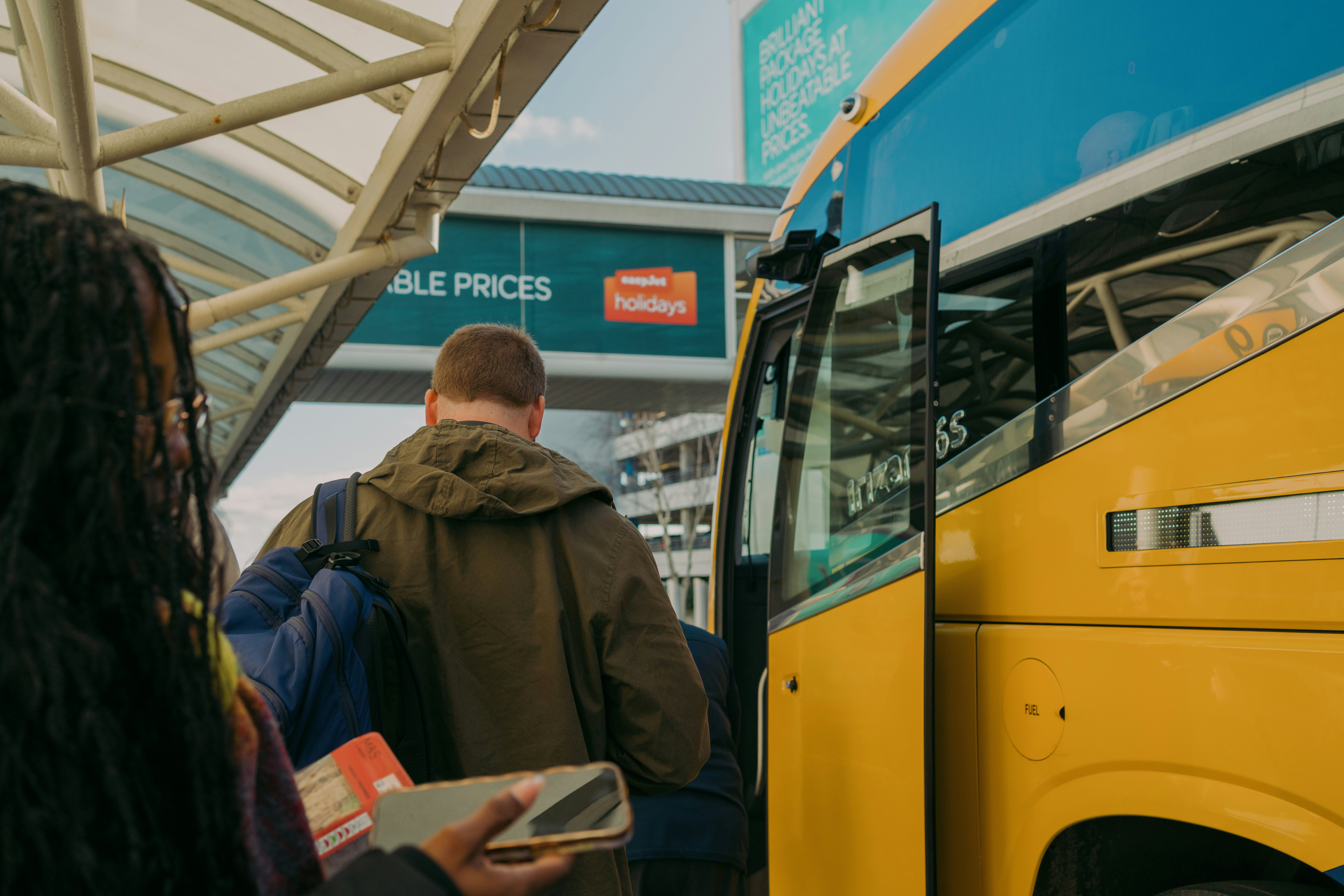 People board a yellow bus at a bus stop.
