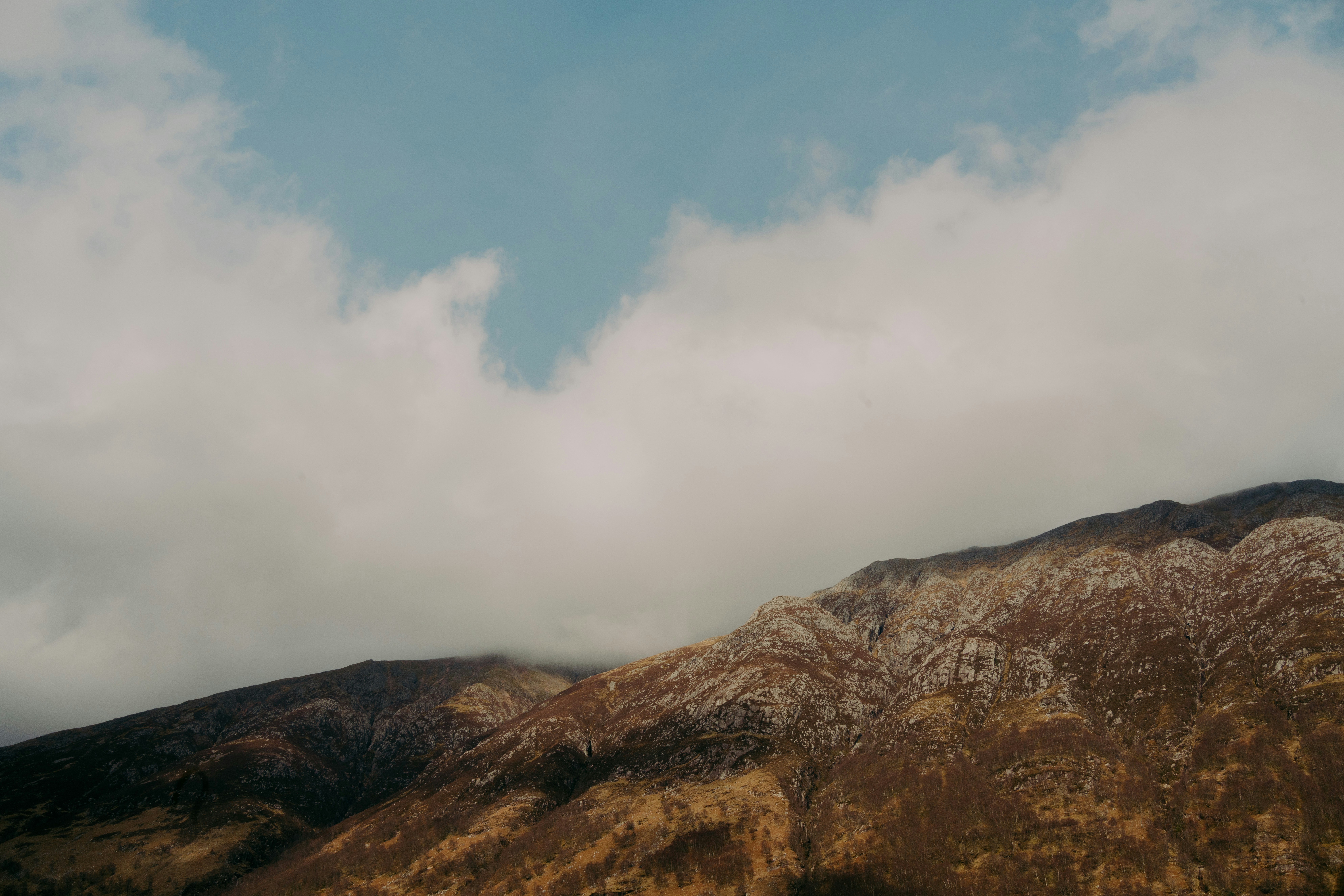 Mountain covered by clouds, with a blue sky above.