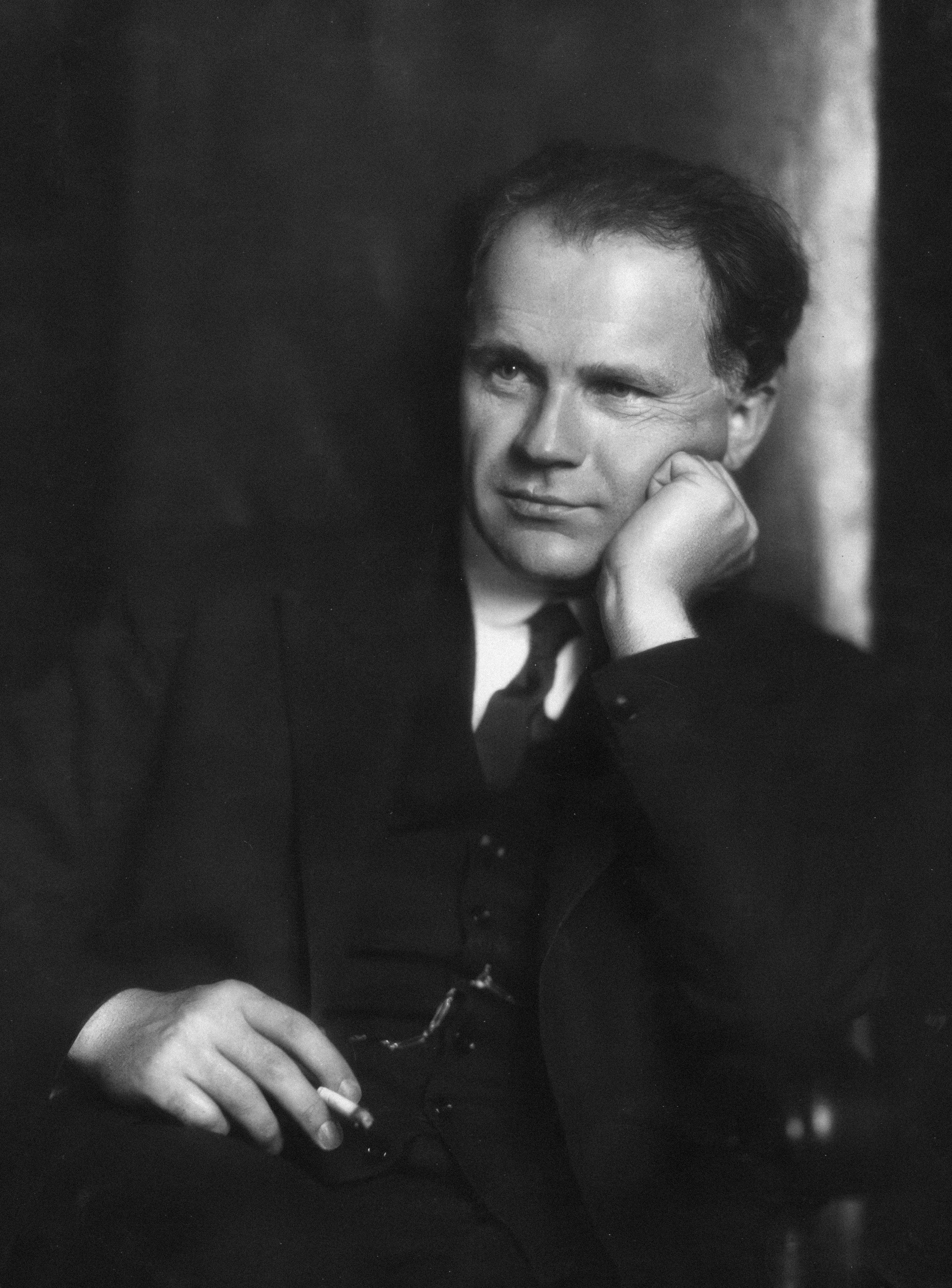 Man in suit resting chin on hand, holding cigarette.