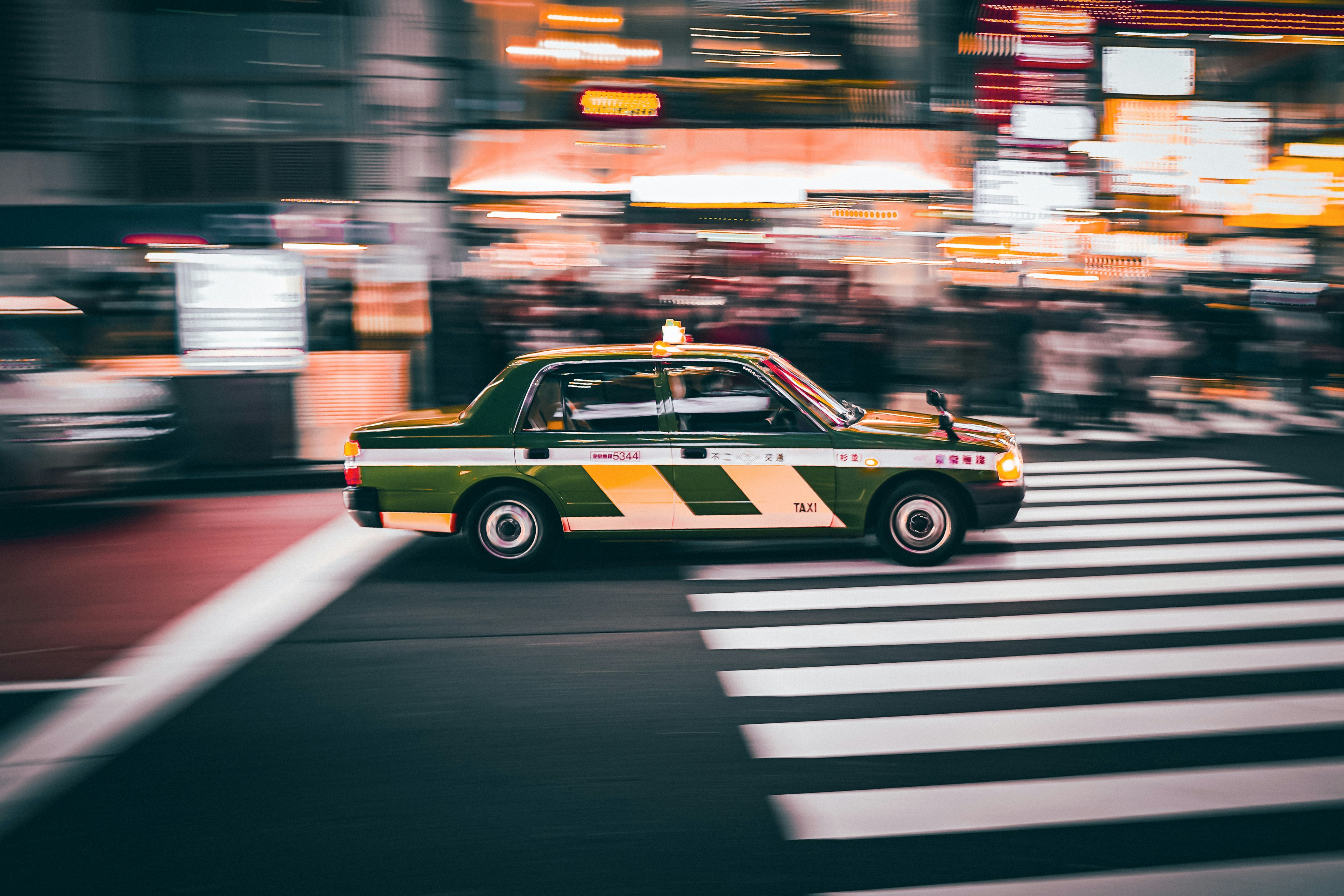 A japanese taxi speeds across a crosswalk.