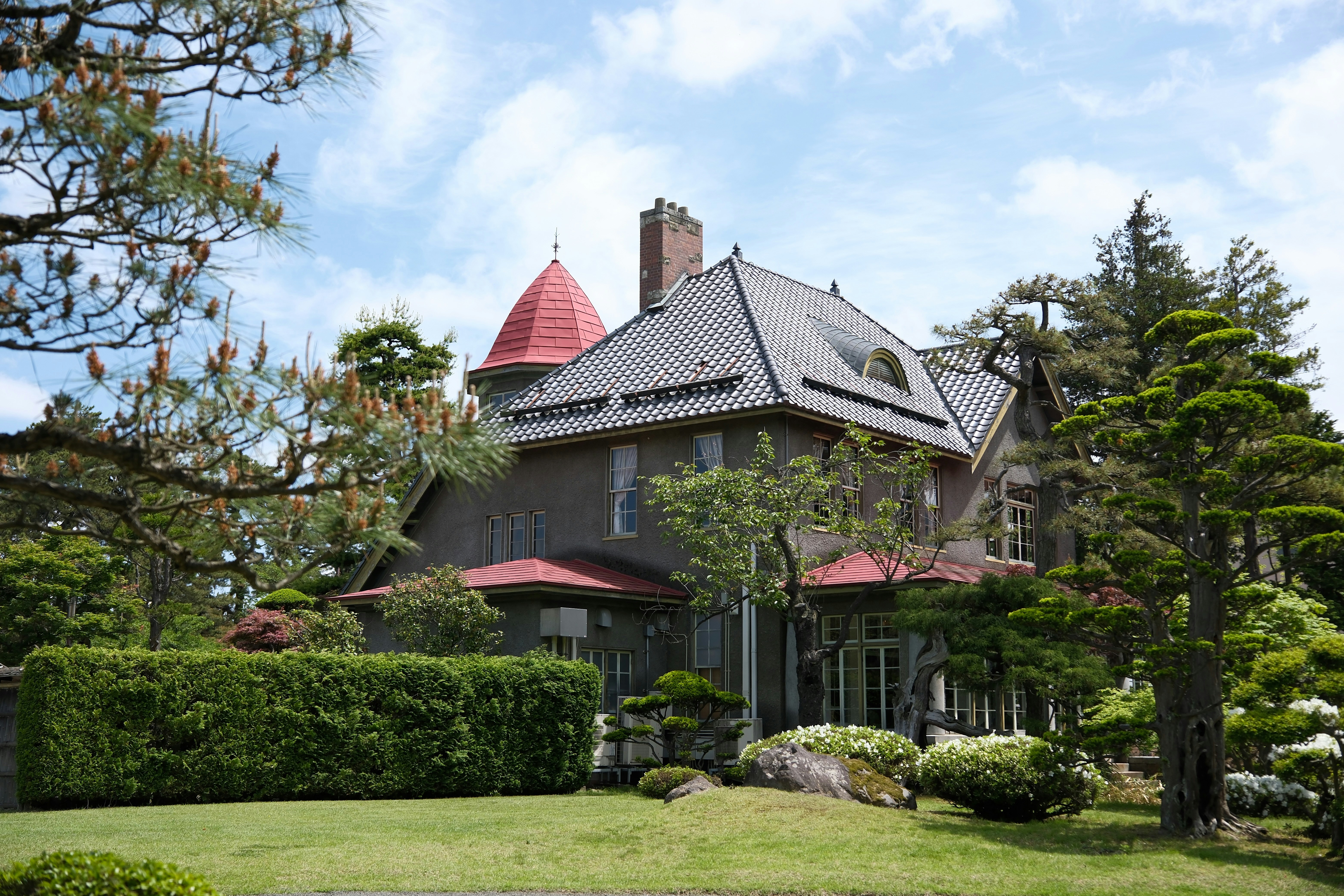 A beautiful house with a red tower and lush gardens.