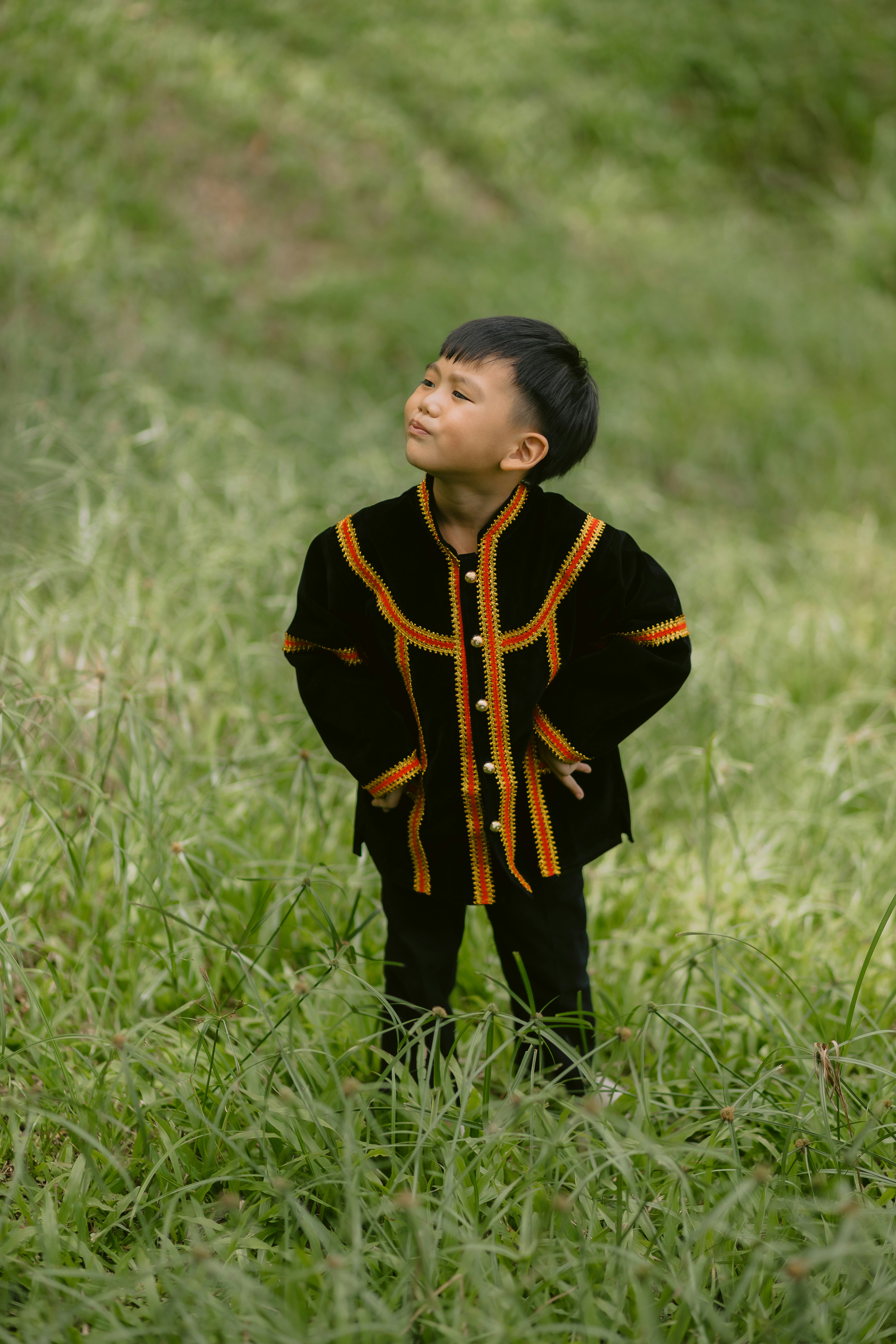 A young boy in traditional attire stands in grass.