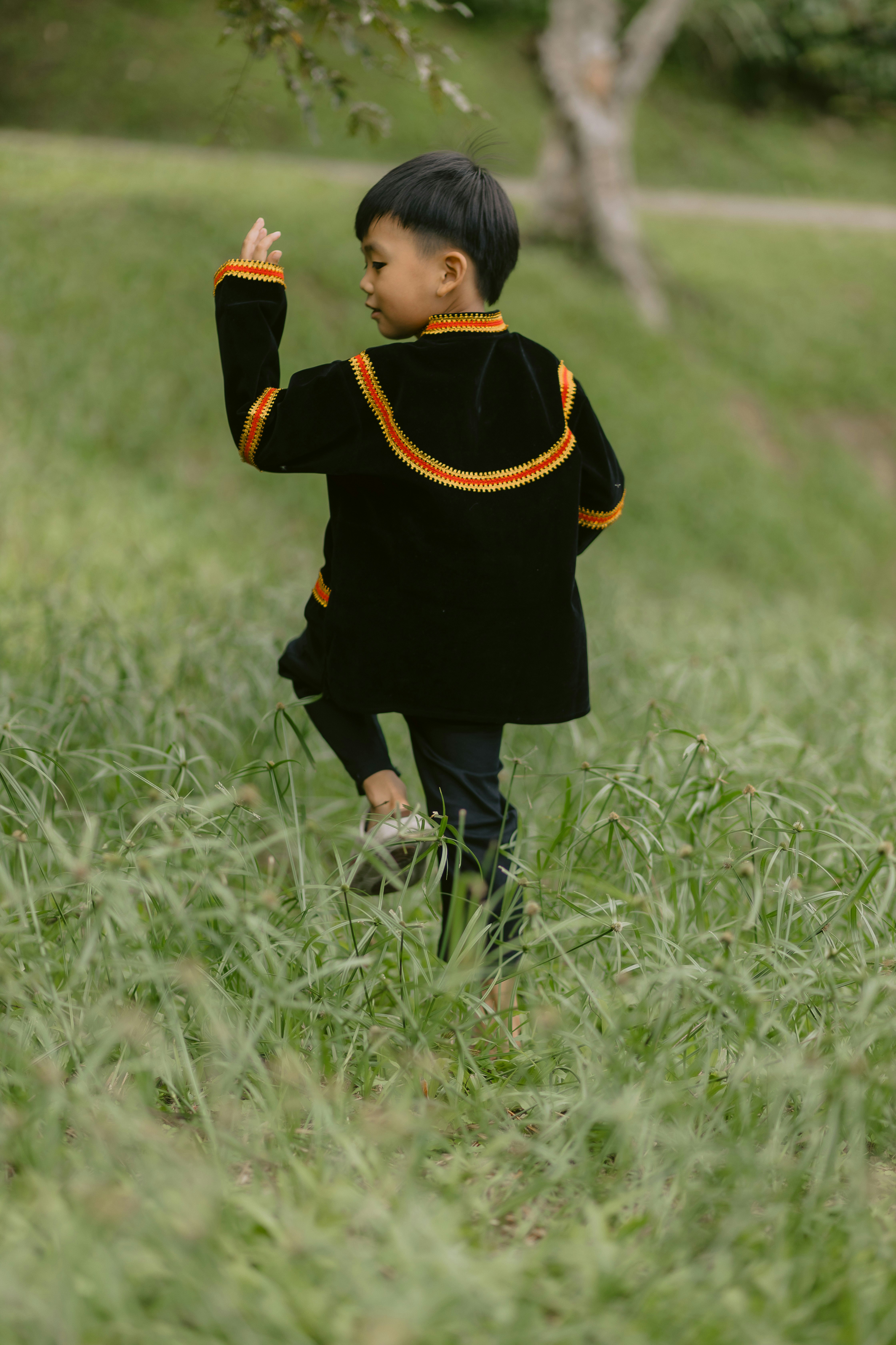 A boy in traditional clothes walks through grass.