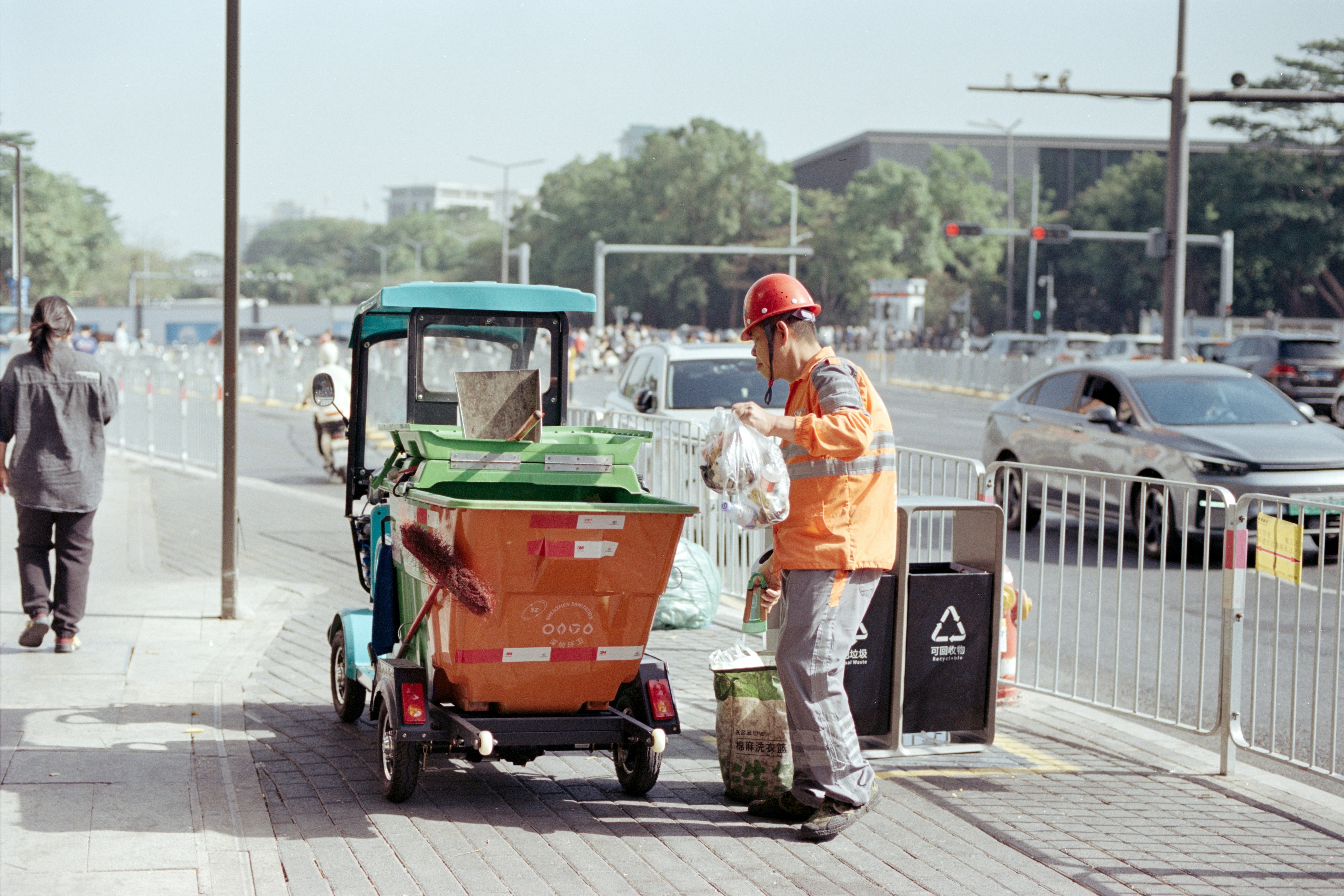 A street cleaner empties trash into a recycling cart.
