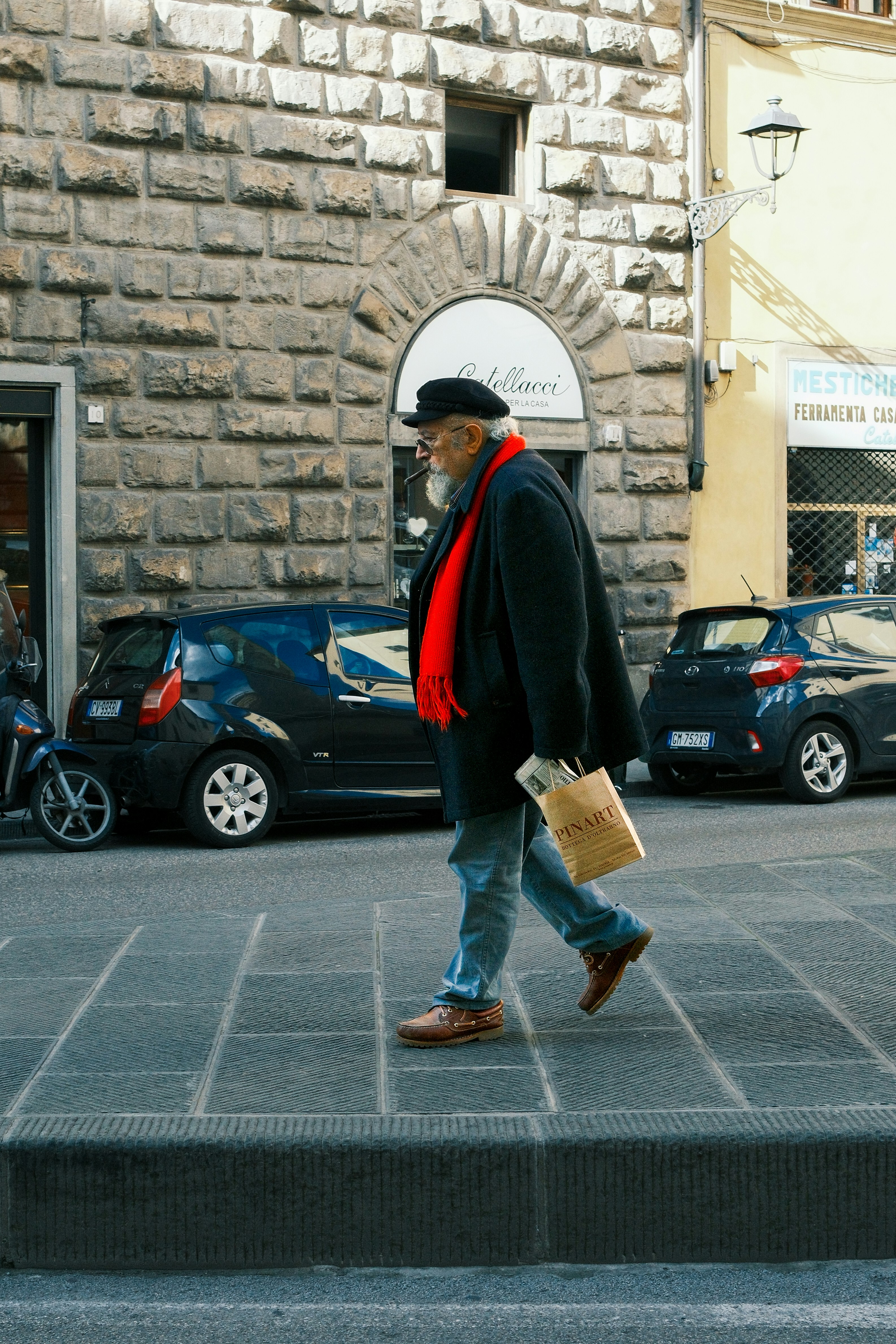 An older man with a striking red scarf walking through the stone streets of Florence. A moment of color and style.