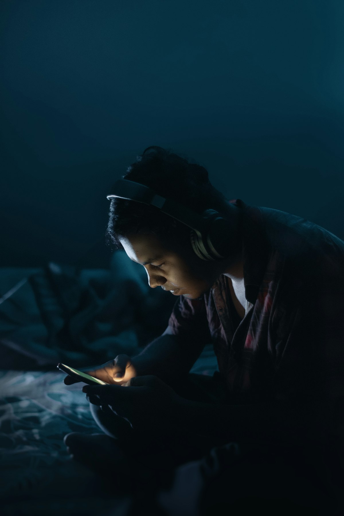 adolescente de fones de ouvido usa o celular no escuro