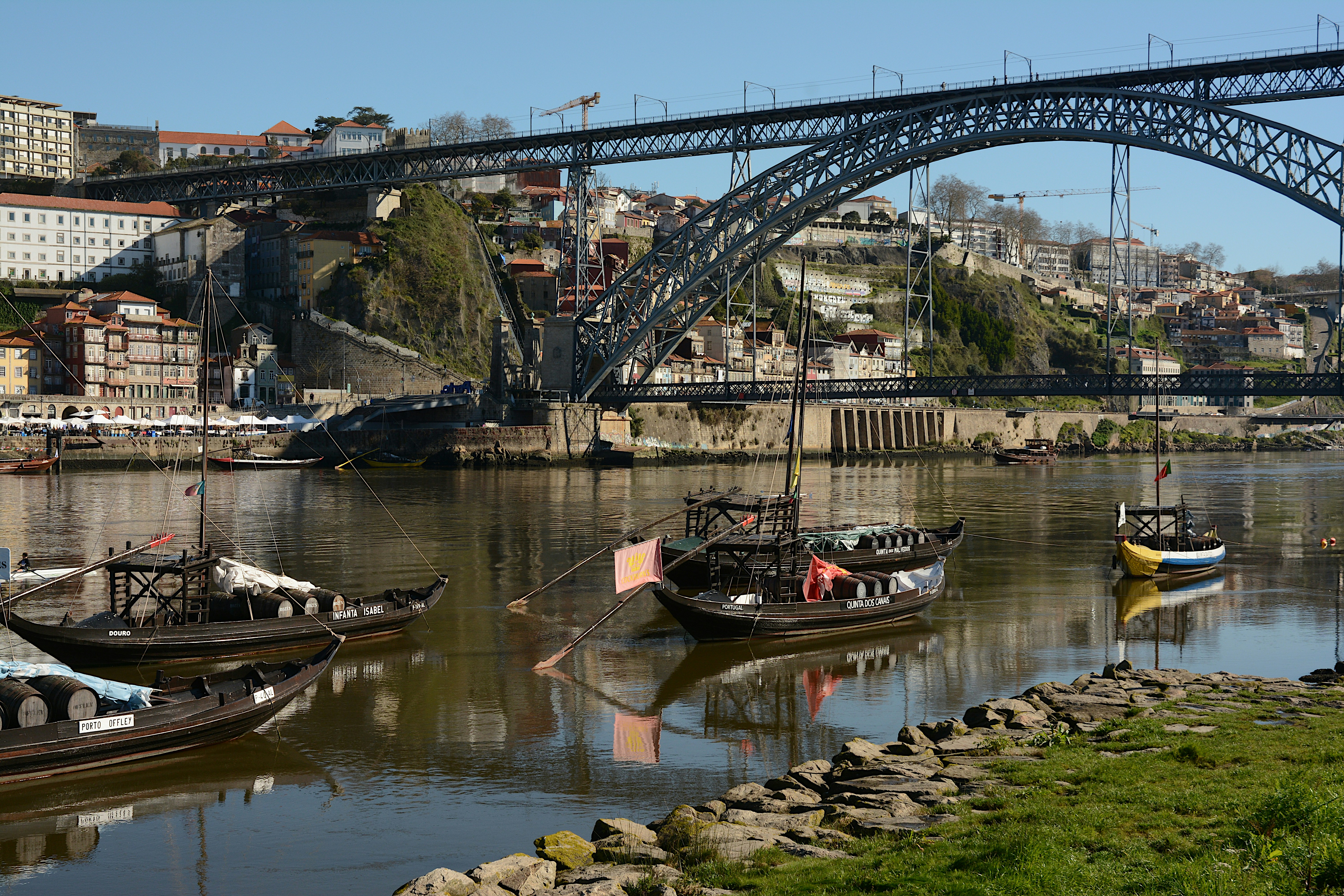 Boats float on a river below a large bridge.