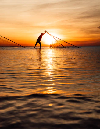 A fisherman casts his net in the sunset.