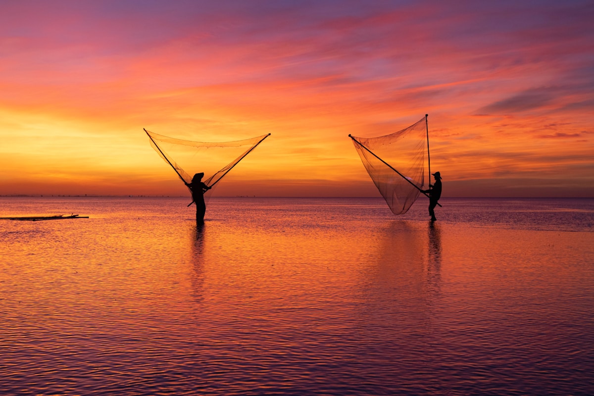 Pescadores lançando redes ao pôr do sol sobre águas calmas — simbolizando a pesca milagrosa de Lucas 5, quando Jesus chamou Simão Pedro e os primeiros discípulos às margens do lago de Genesaré, rompendo convenções religiosas e sociais para convidar pecadores ao arrependimento