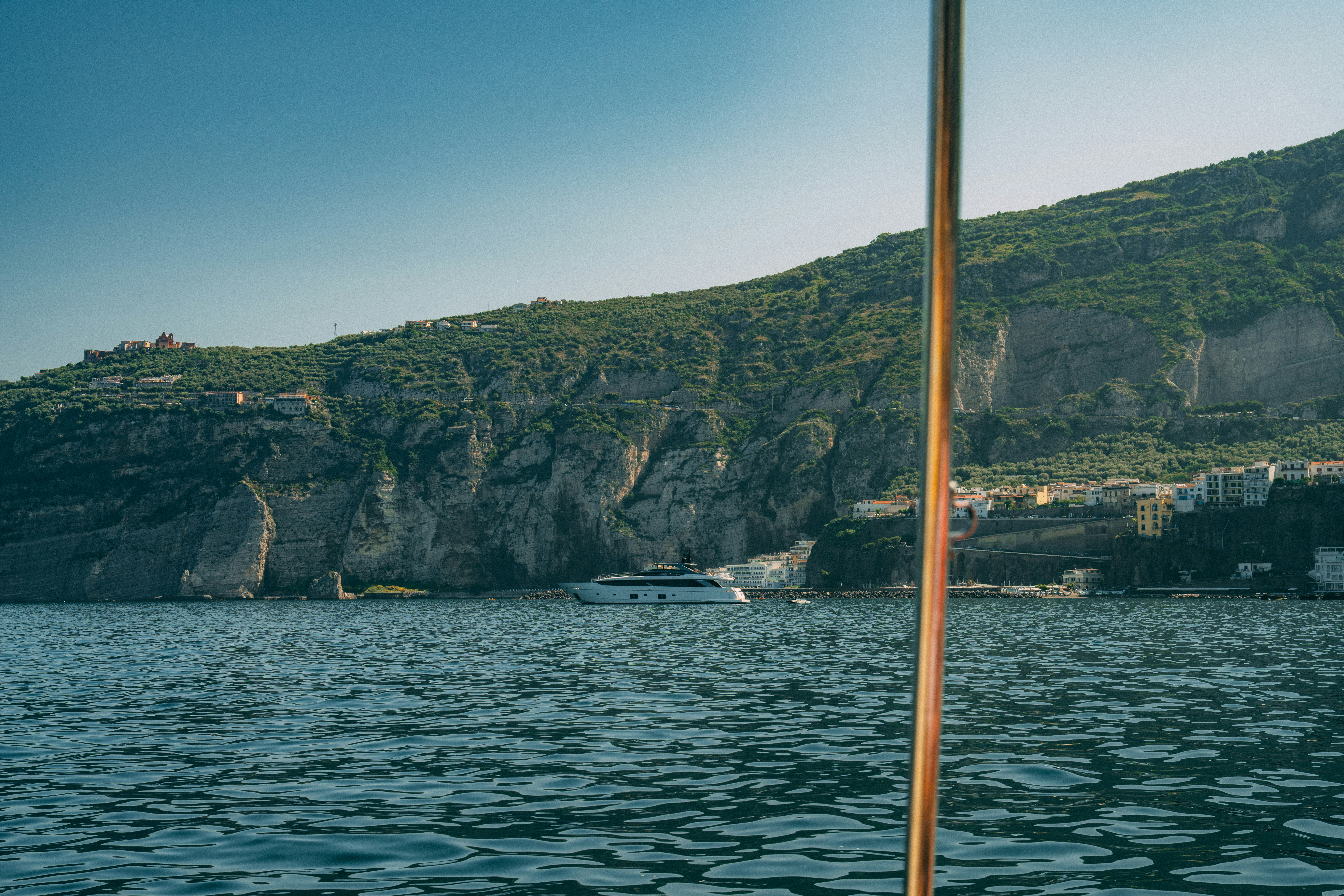 A boat sails near a mountainous coastline