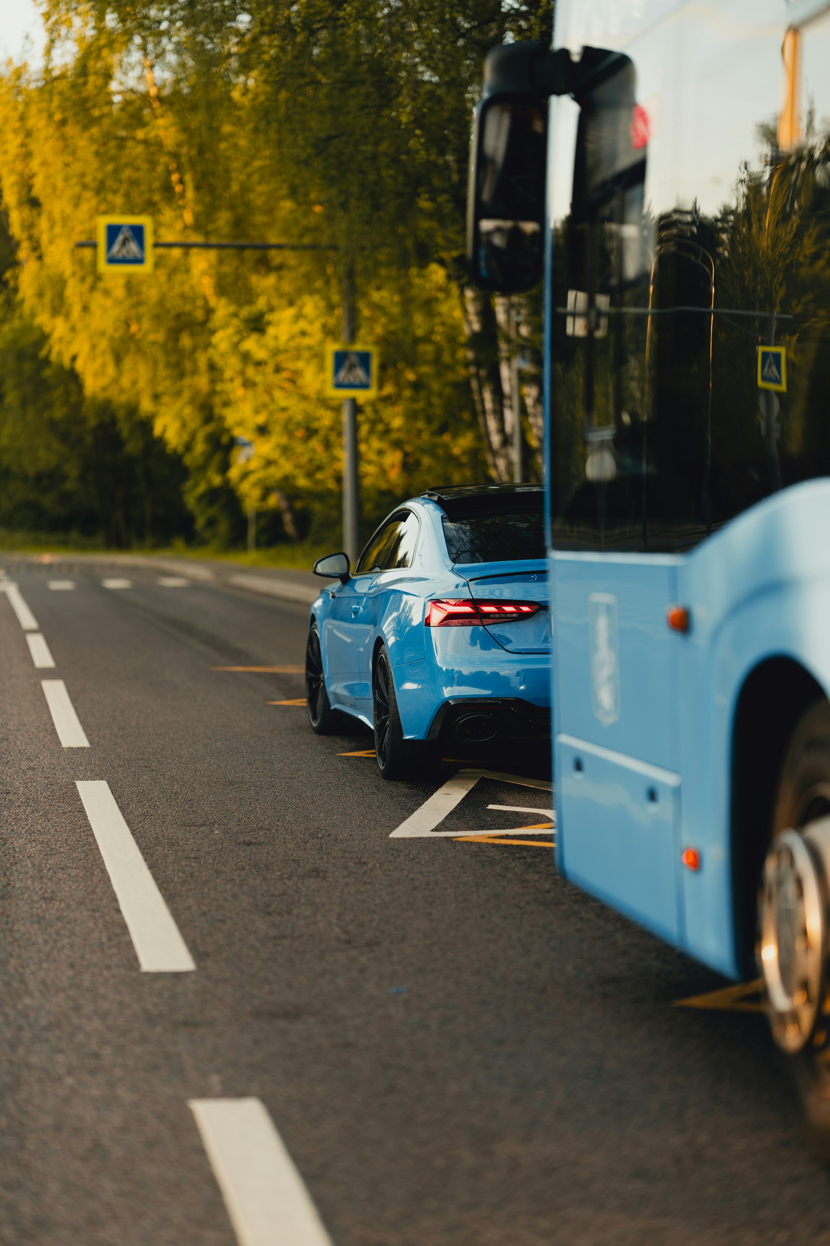A blue car parked next to a bus.