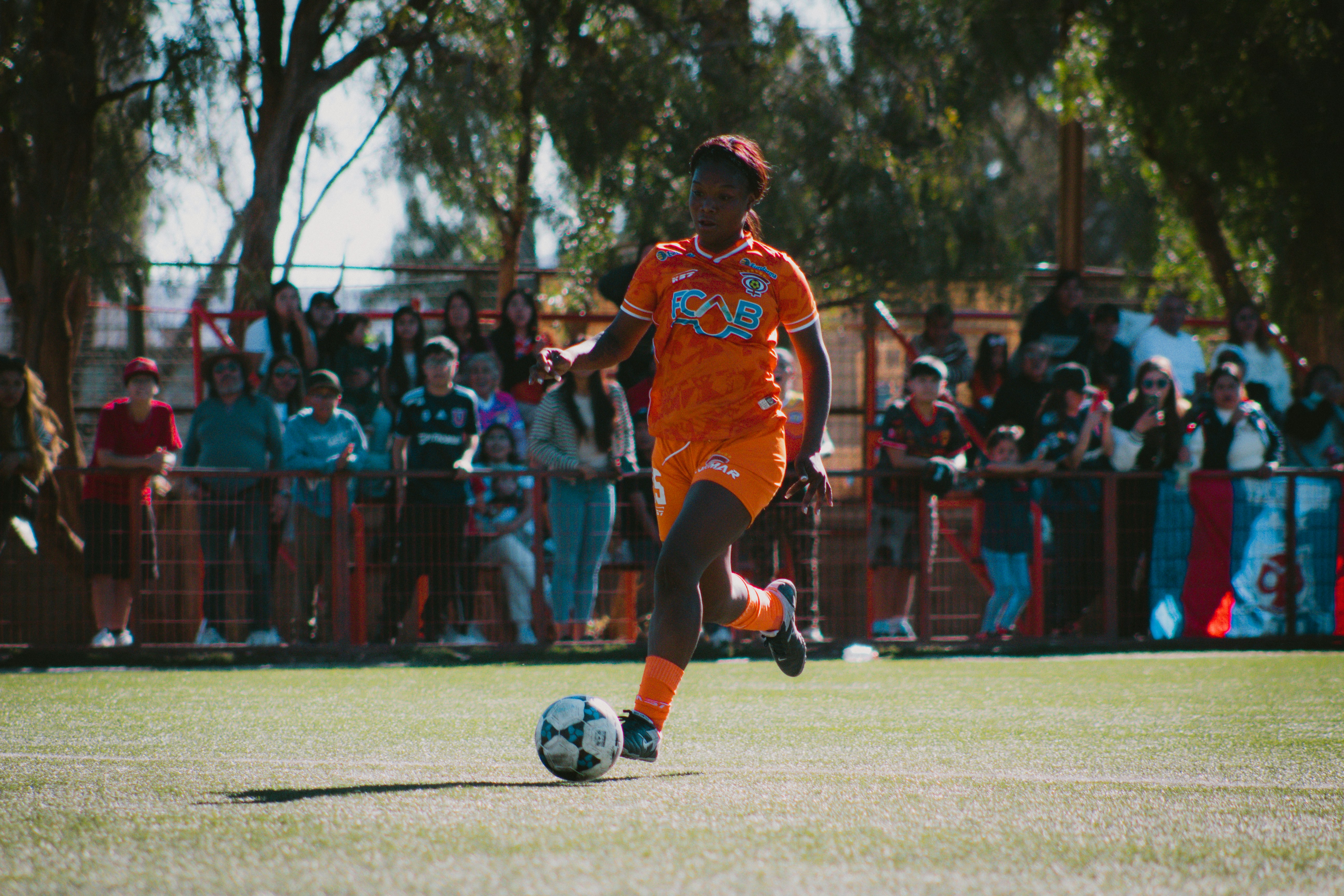 Ein Fußballspieler dribbelt den Ball auf einem sonnigen Feld.