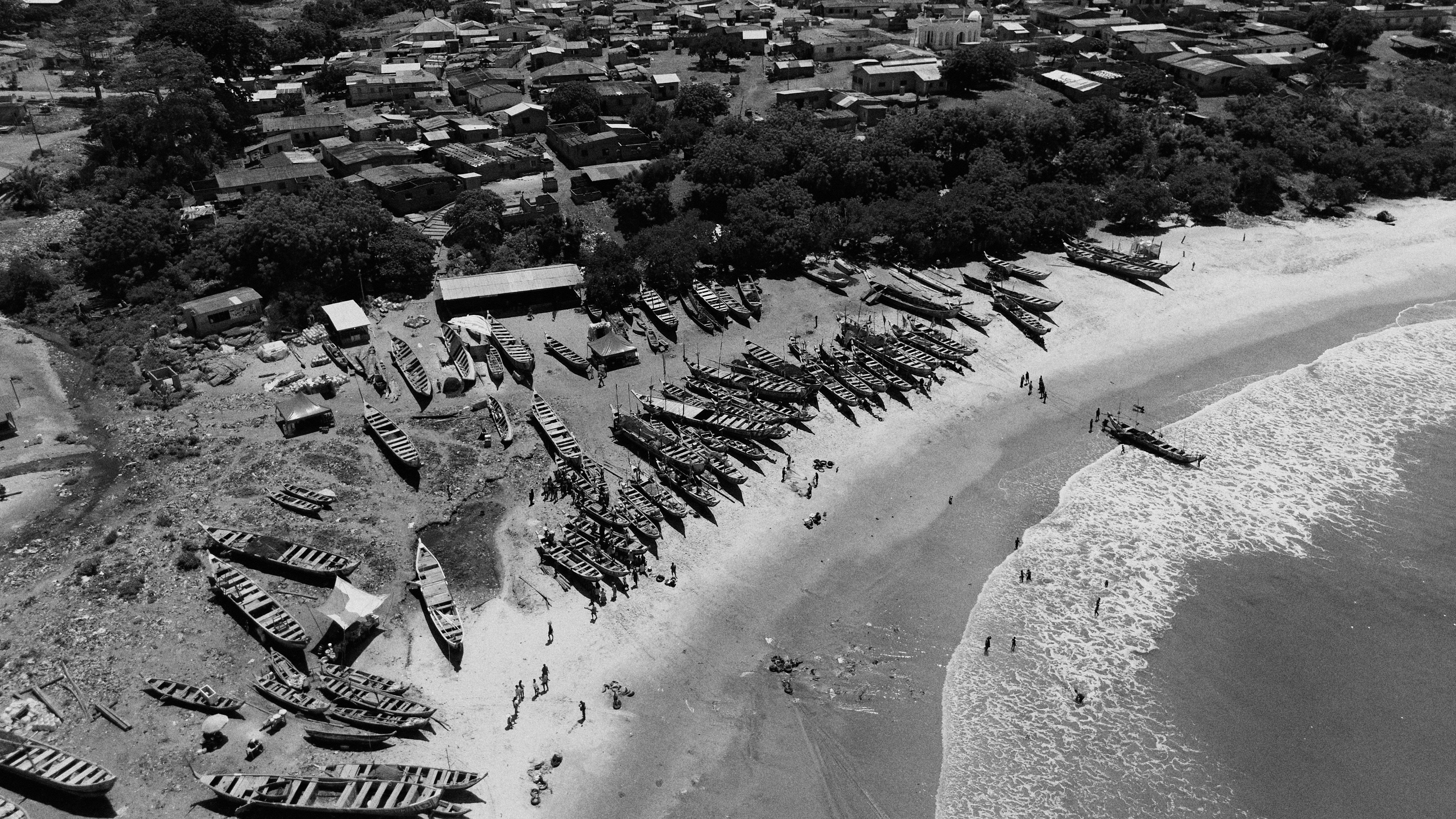 Boats lined up on a sandy beach near a town.