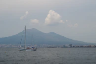 A sailboat glides past a mountain on the sea.