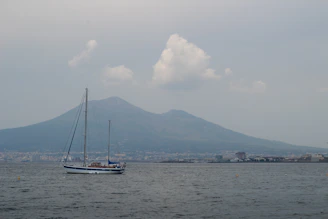 A sailboat glides past a mountain on the sea.