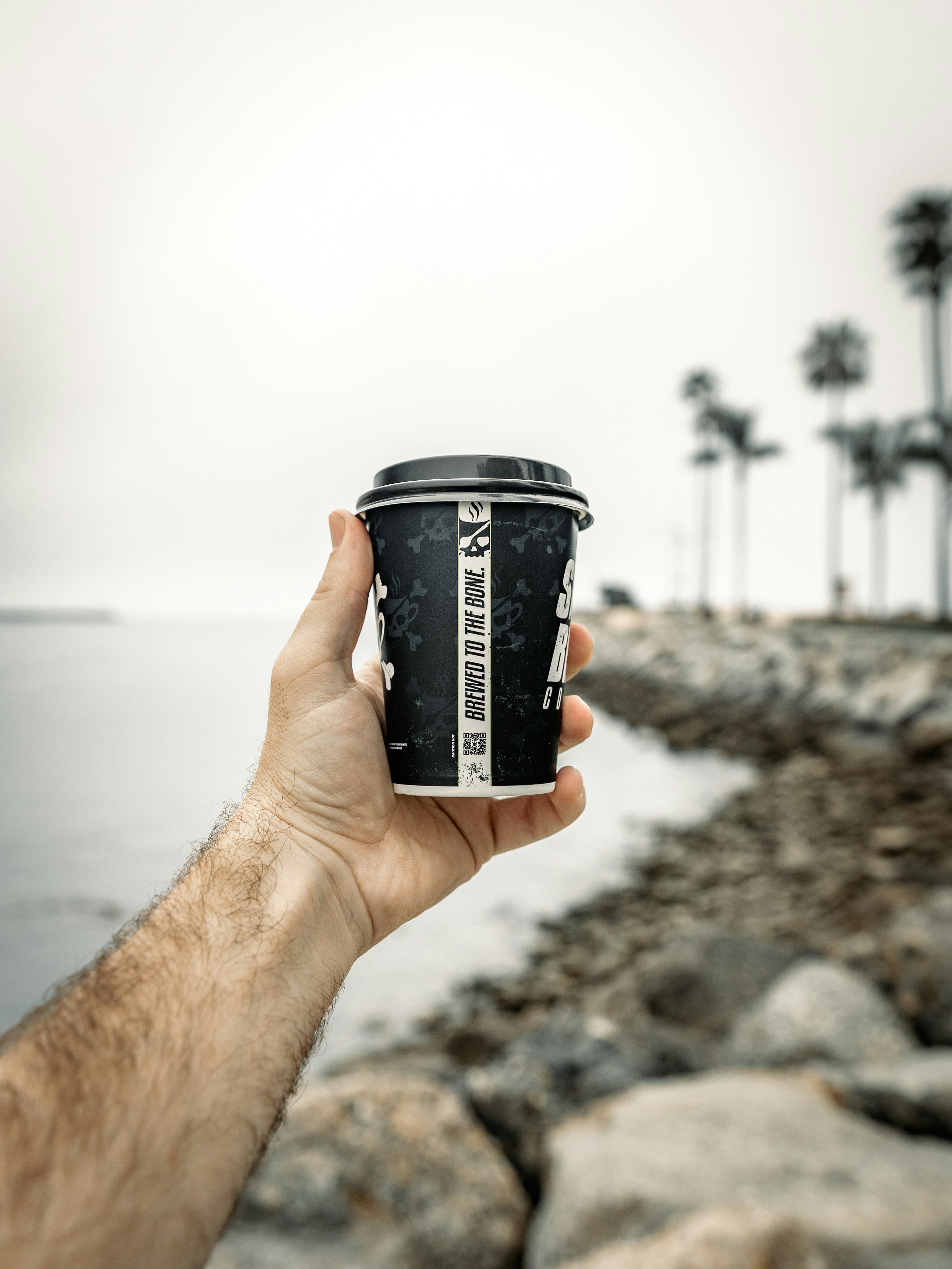 Holding a coffee cup by the ocean.
