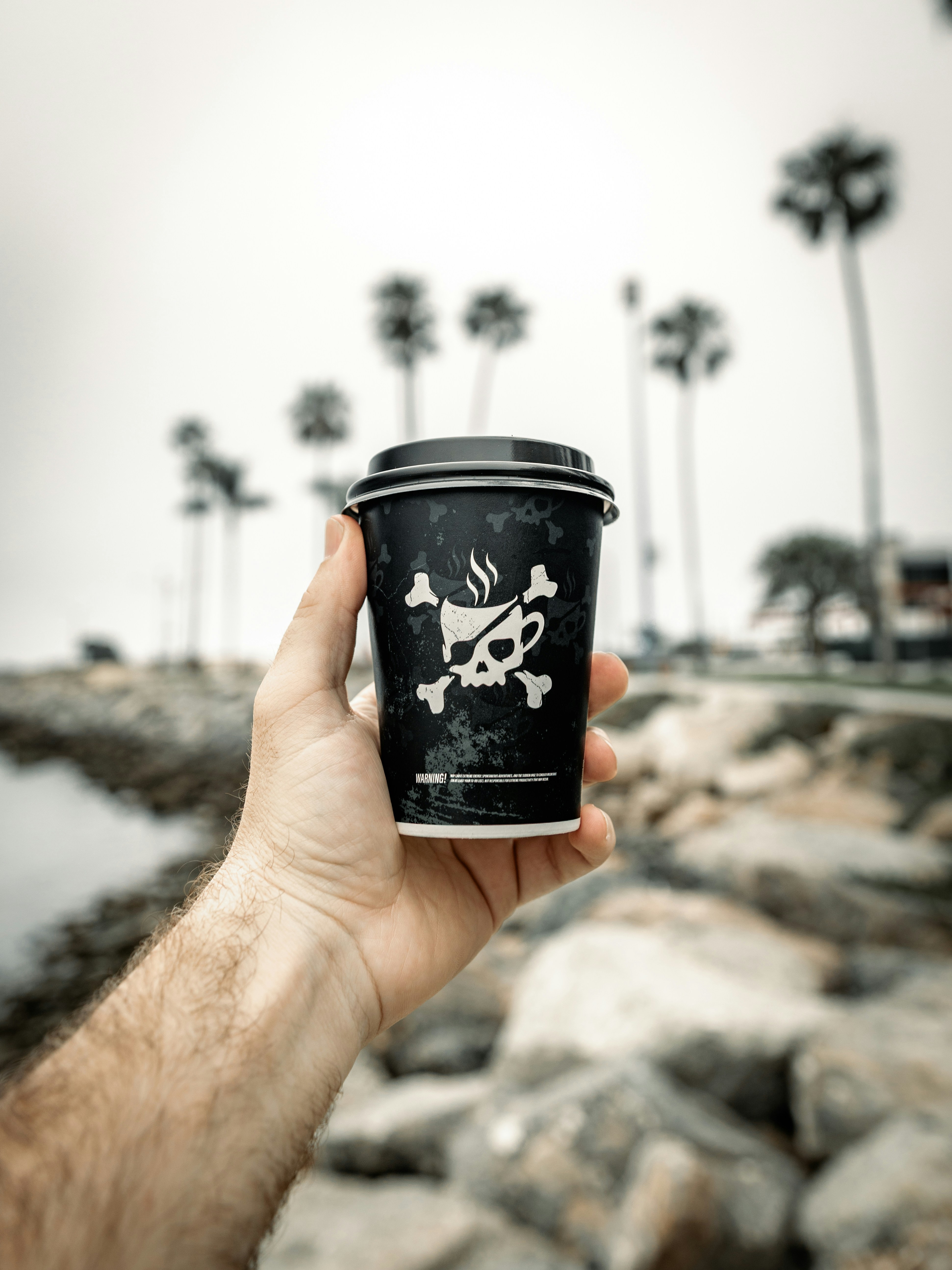 A hand holds a coffee cup with a skull.