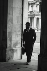 A dapper man walks through an archway.