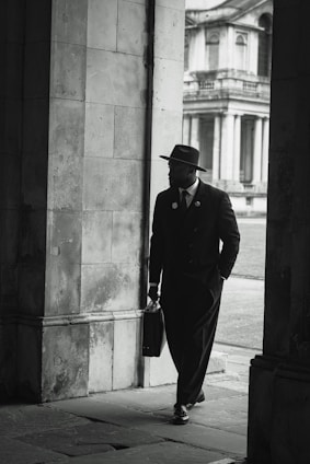 A dapper man walks through an archway.