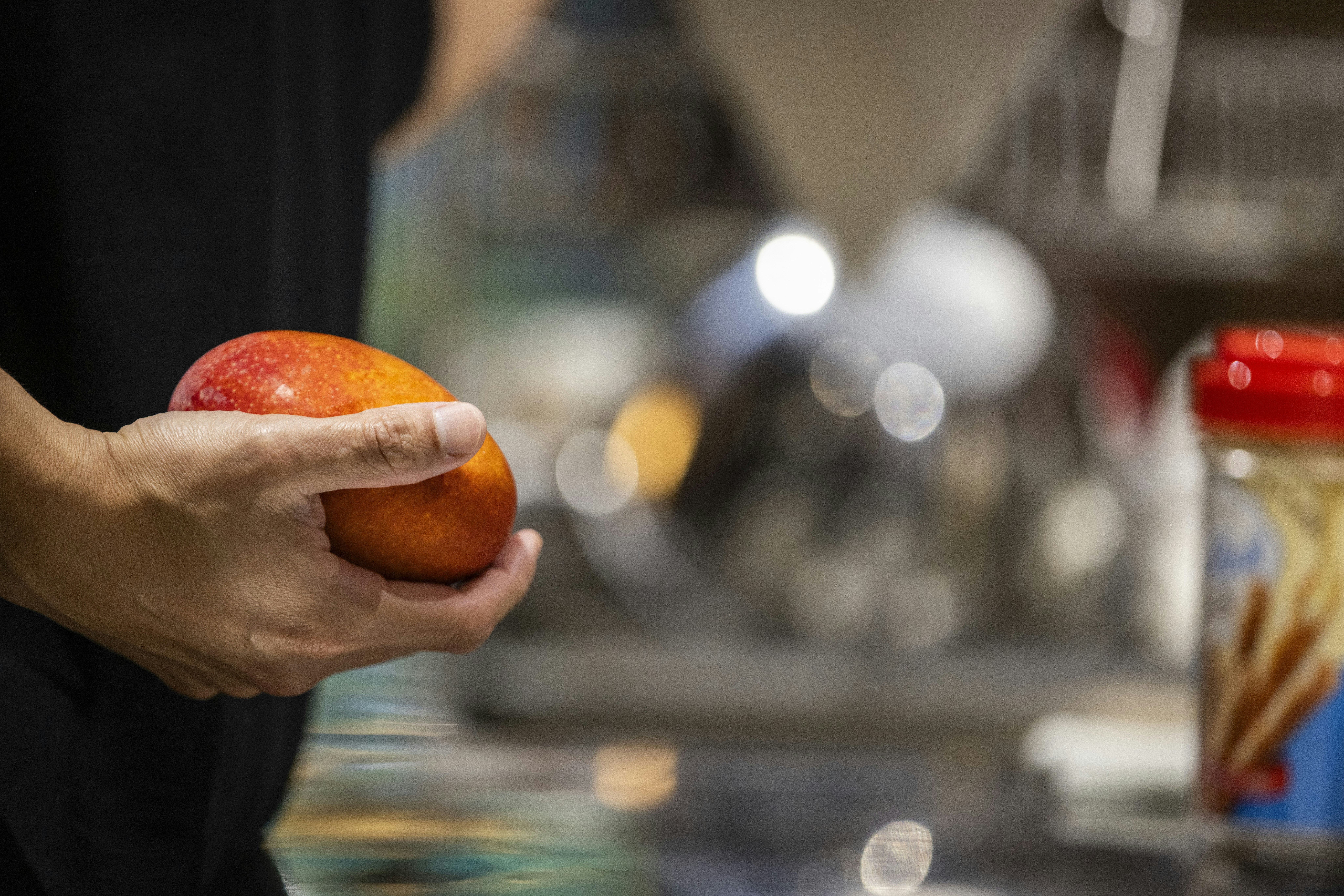 A person is holding a ripe, red mango.