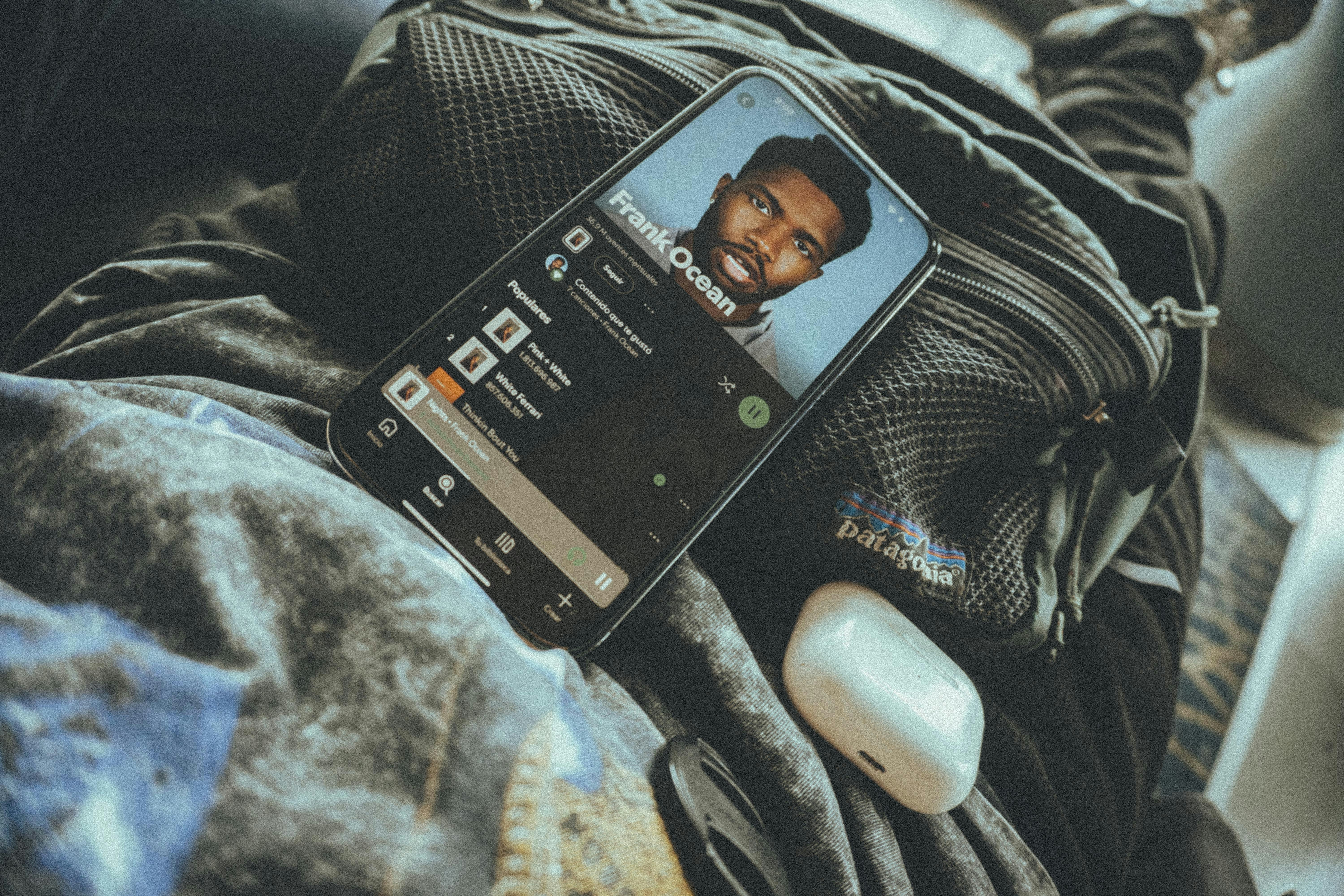 A phone and airpods rest on a backpack.