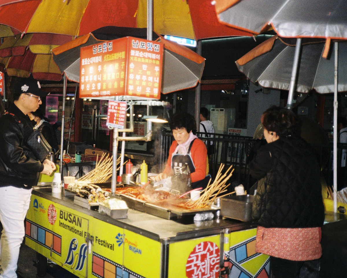 Vendor cooking at a Busan street food stall under market umbrellas
