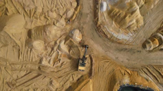 An excavator works in a sandy terrain.