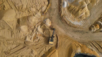 An excavator works in a sandy terrain.