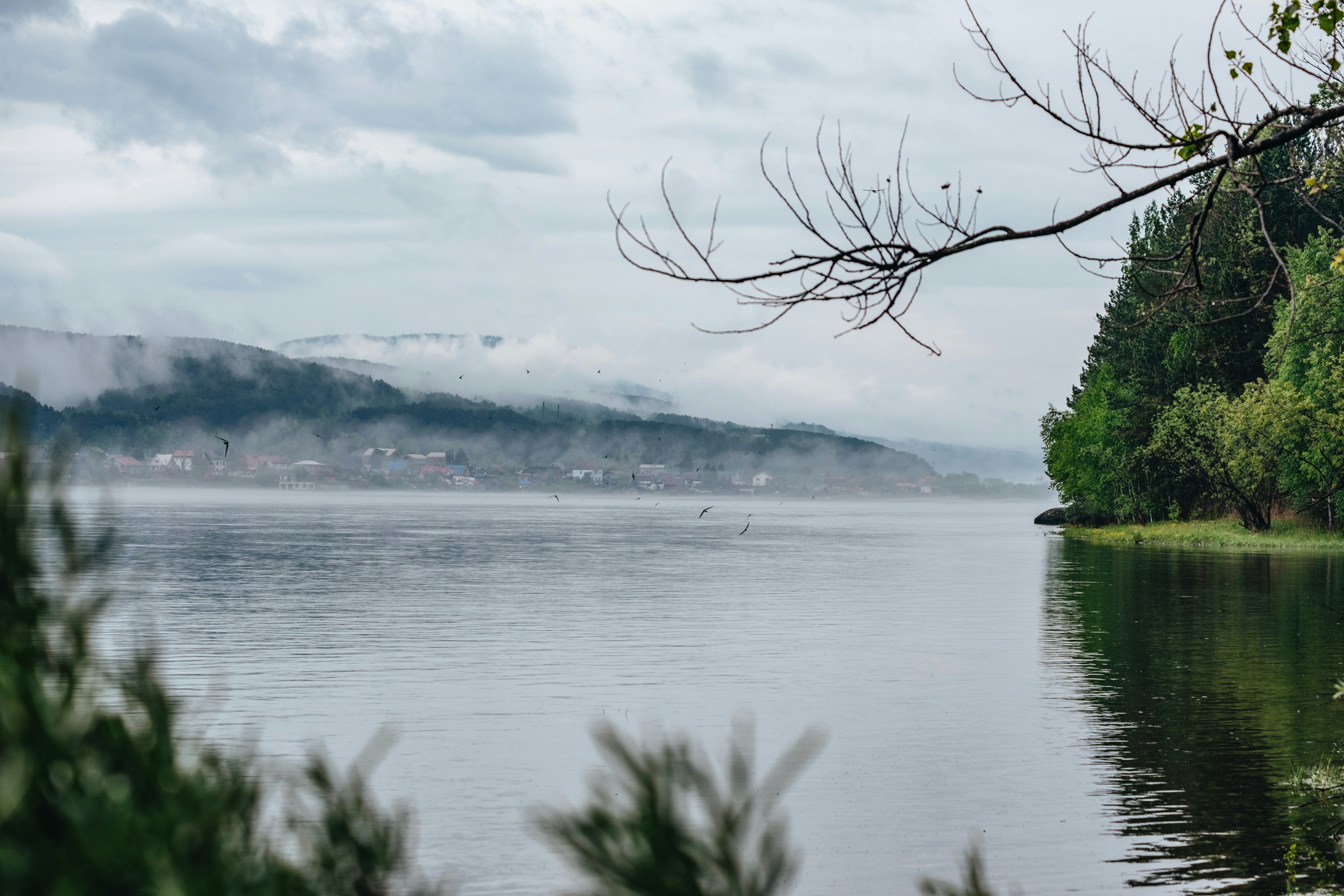 A calm lake is surrounded by foggy mountains.