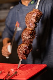 Chef presenting roasted meat on a skewer.