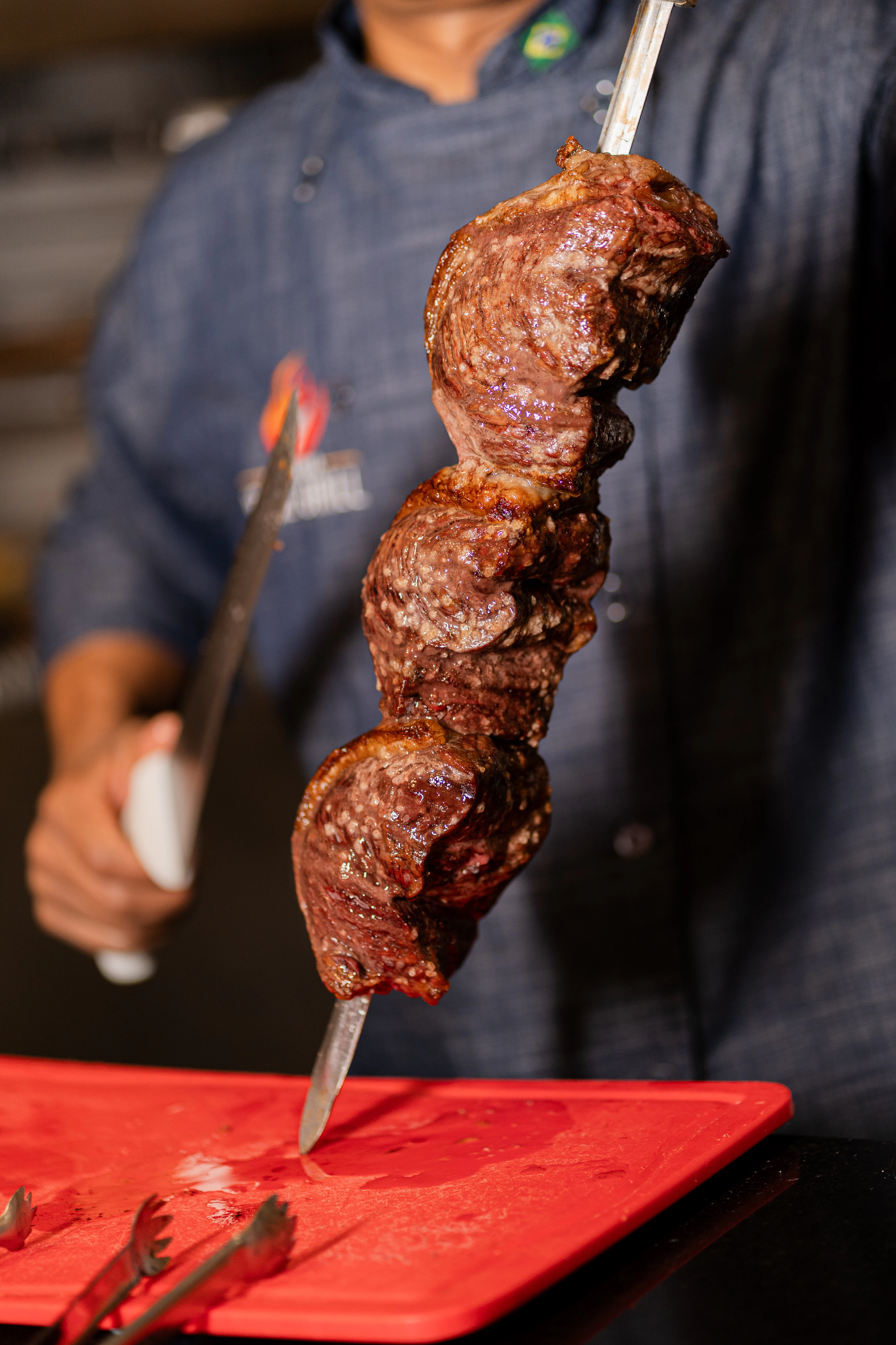 A grill chef presenting a skewer of picanha carved rodizio-style, the centrepiece cut of Brazilian churrasco.