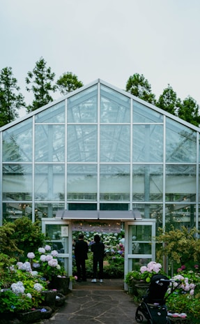 People stand before a greenhouse entrance filled with flowers.