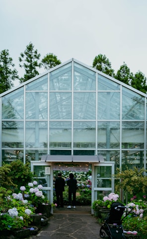 People stand before a greenhouse entrance filled with flowers.
