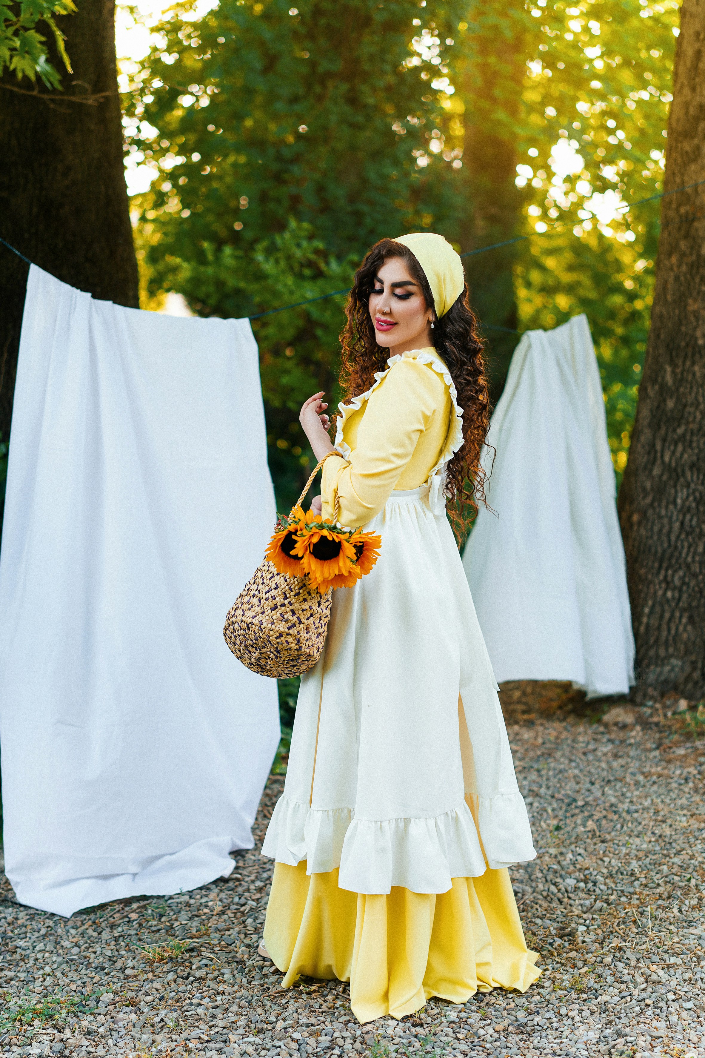 A woman poses with sunflowers near drying laundry.