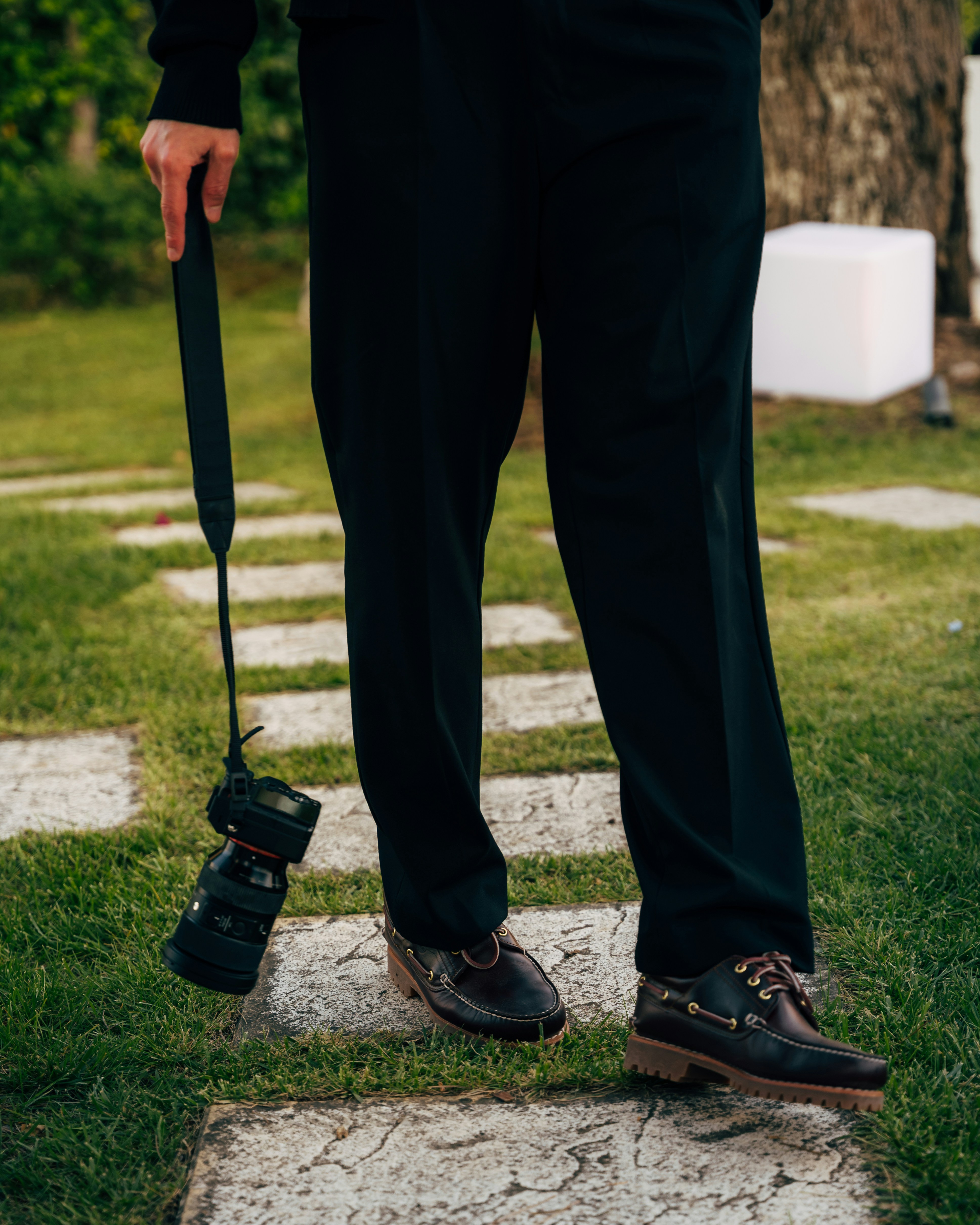 Photographer holds a camera, walking on stone path.