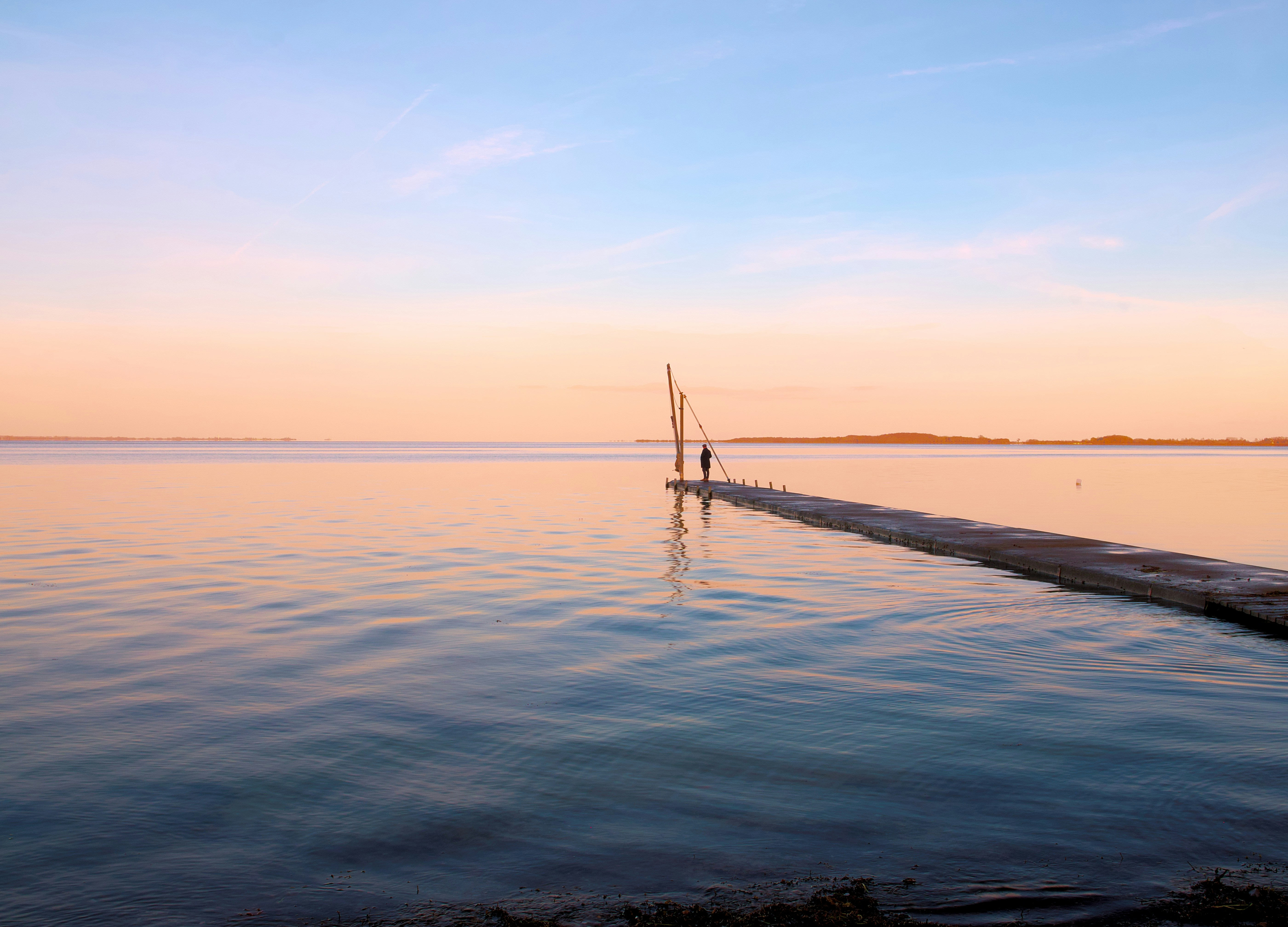 People stand at the end of a dock at sunset.