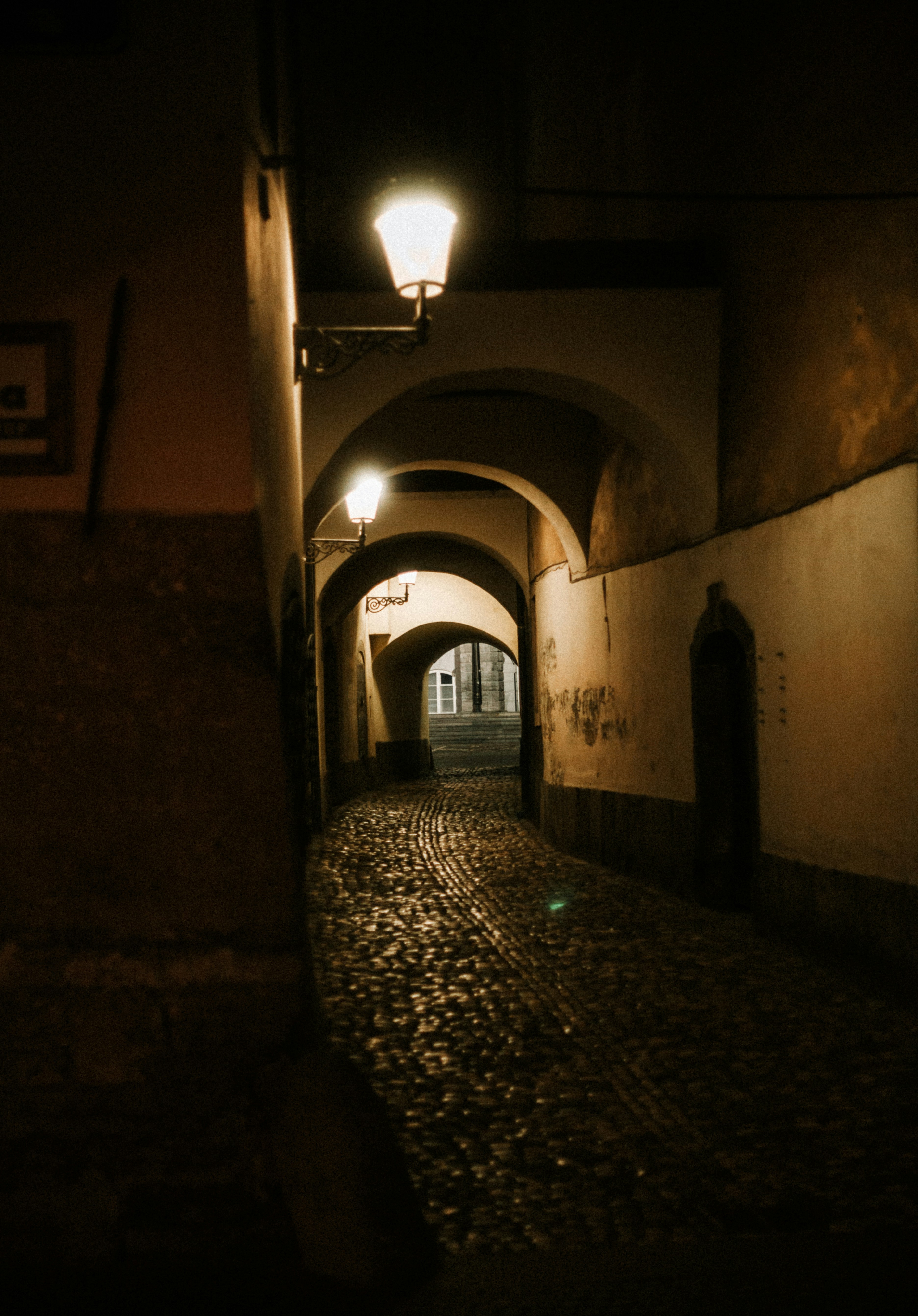 A dark, cobbled alleyway is illuminated by streetlights.