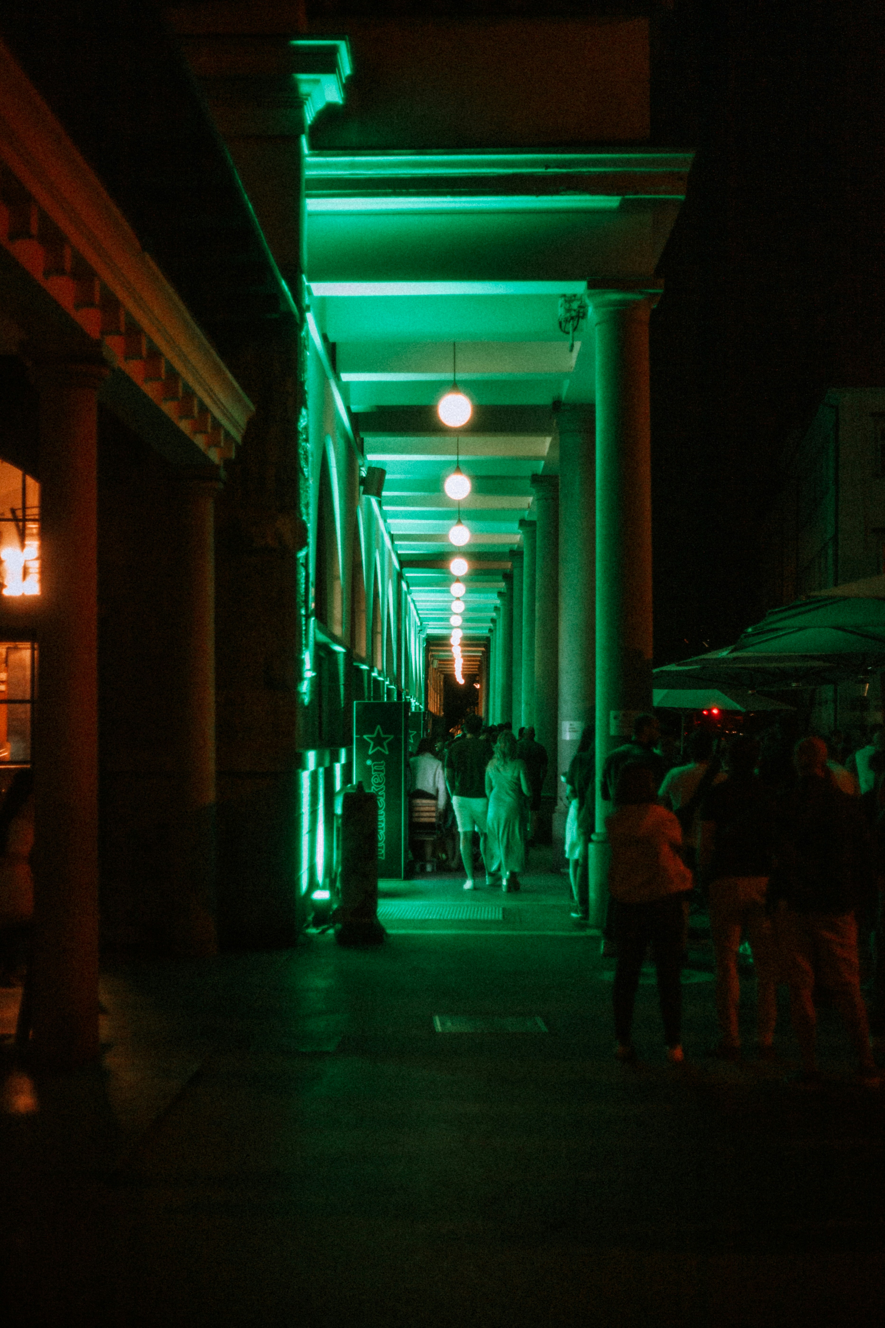 Green-lit colonnade with people walking at night.