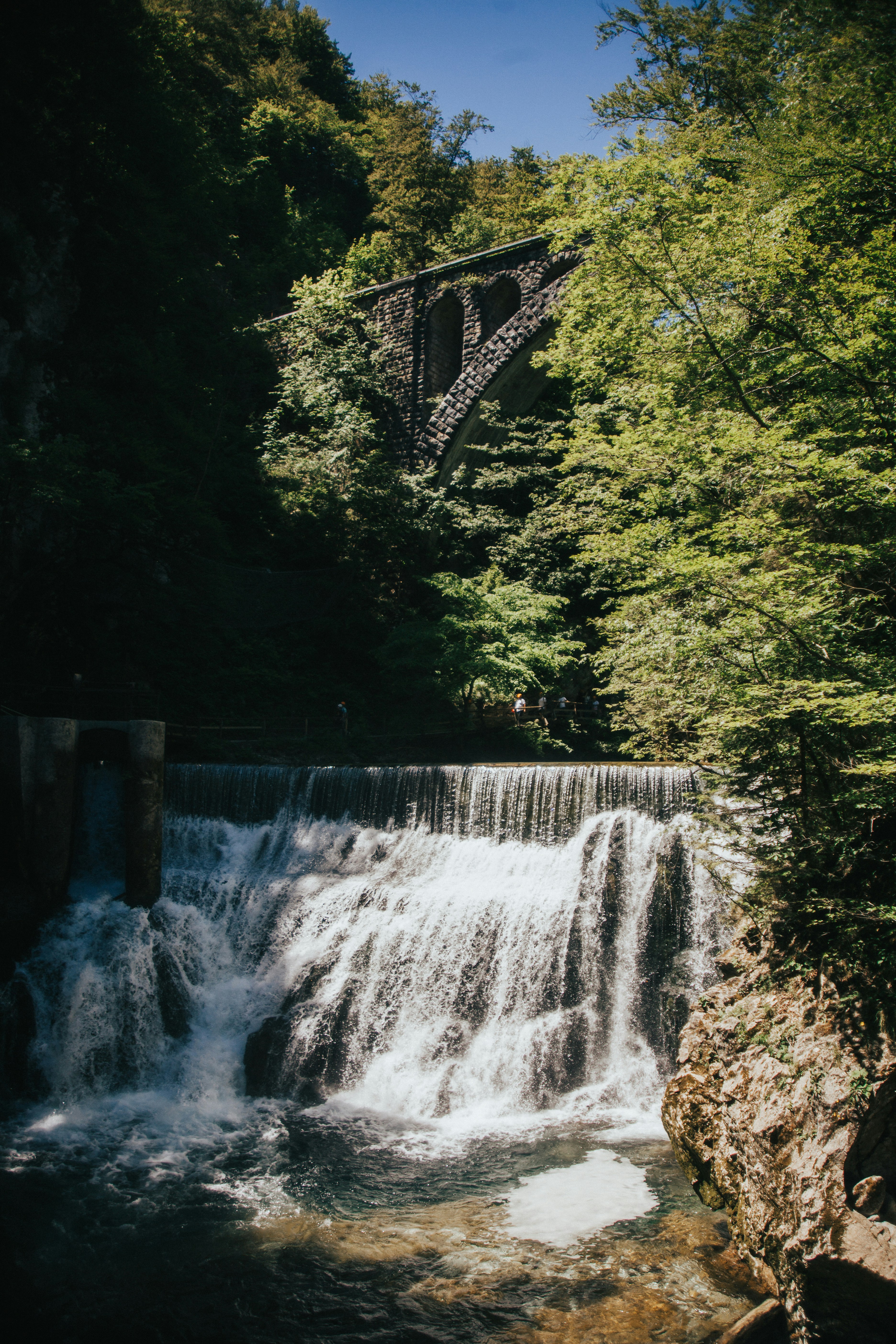 Waterfall flows beneath a historic bridge.