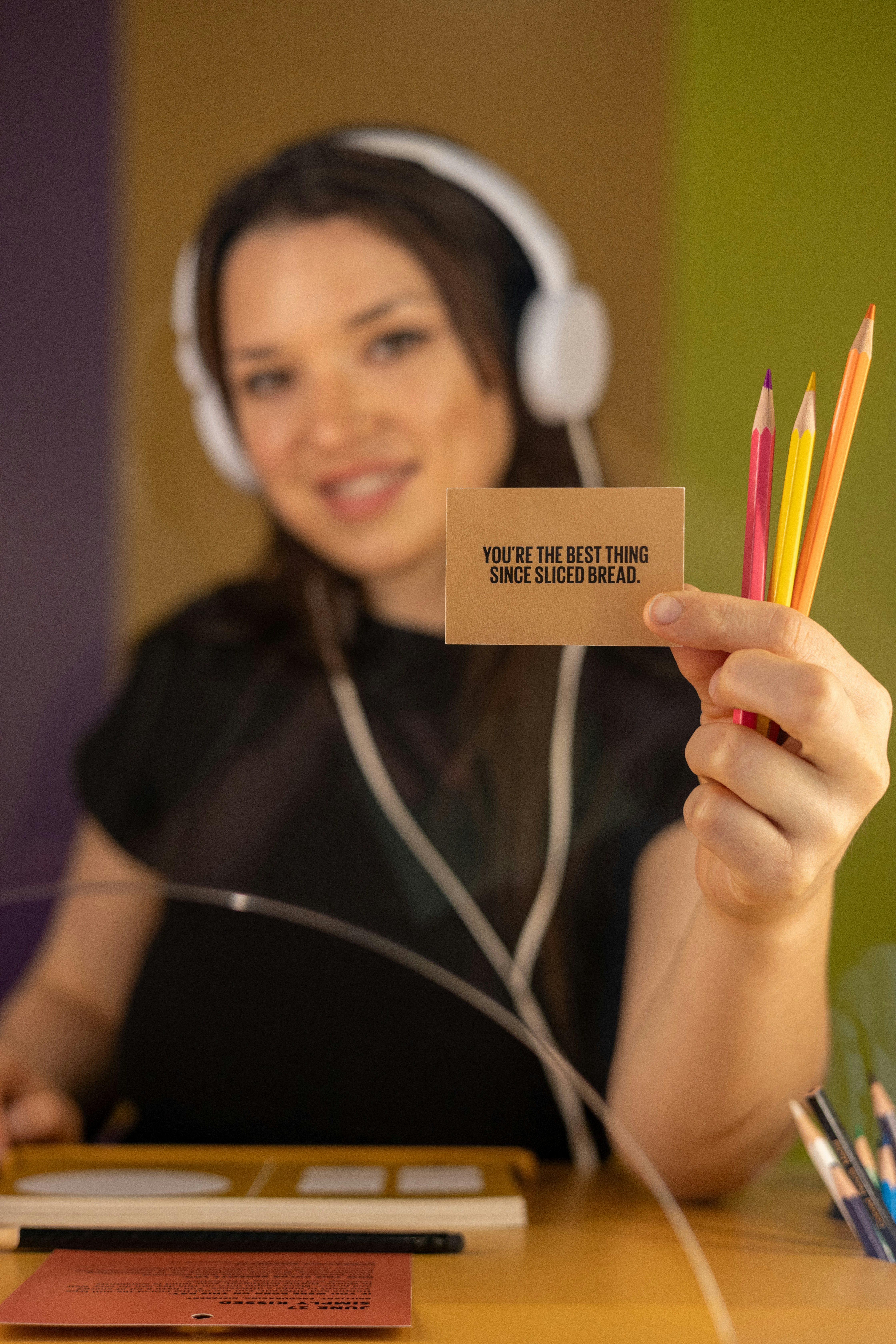 Woman shows card saying "best thing" and colorful pencils.